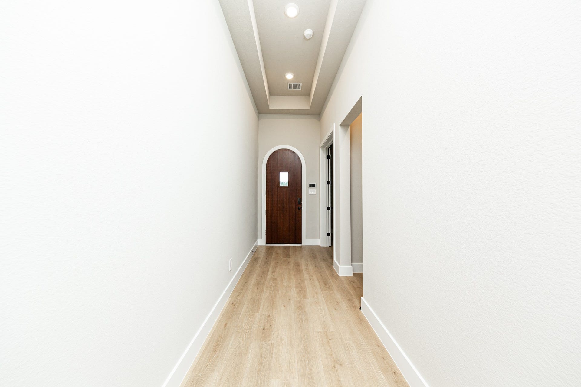 41418 Threadgill Way, Montgomery, TX 77316 This long entryway features wood-look flooring and a tray ceiling. This Spanish-style front door serves as a bold architectural focal point, featuring a classic round arch top and a rich, dark-stained wood finish that provides a deep contrast against the home's light-colored walls
