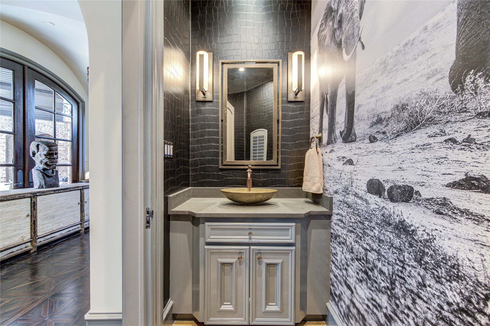 5110 W Oak Mews, Houston, TX 77056 The first-floor powder room makes a bold design statement with its sophisticated African-inspired aesthetic, designer wall finishes, and elegant sconces that cast a warm, inviting glow. This thoughtfully curated space blends artistic character with refined luxury, creating an unforgettable impression for guests.