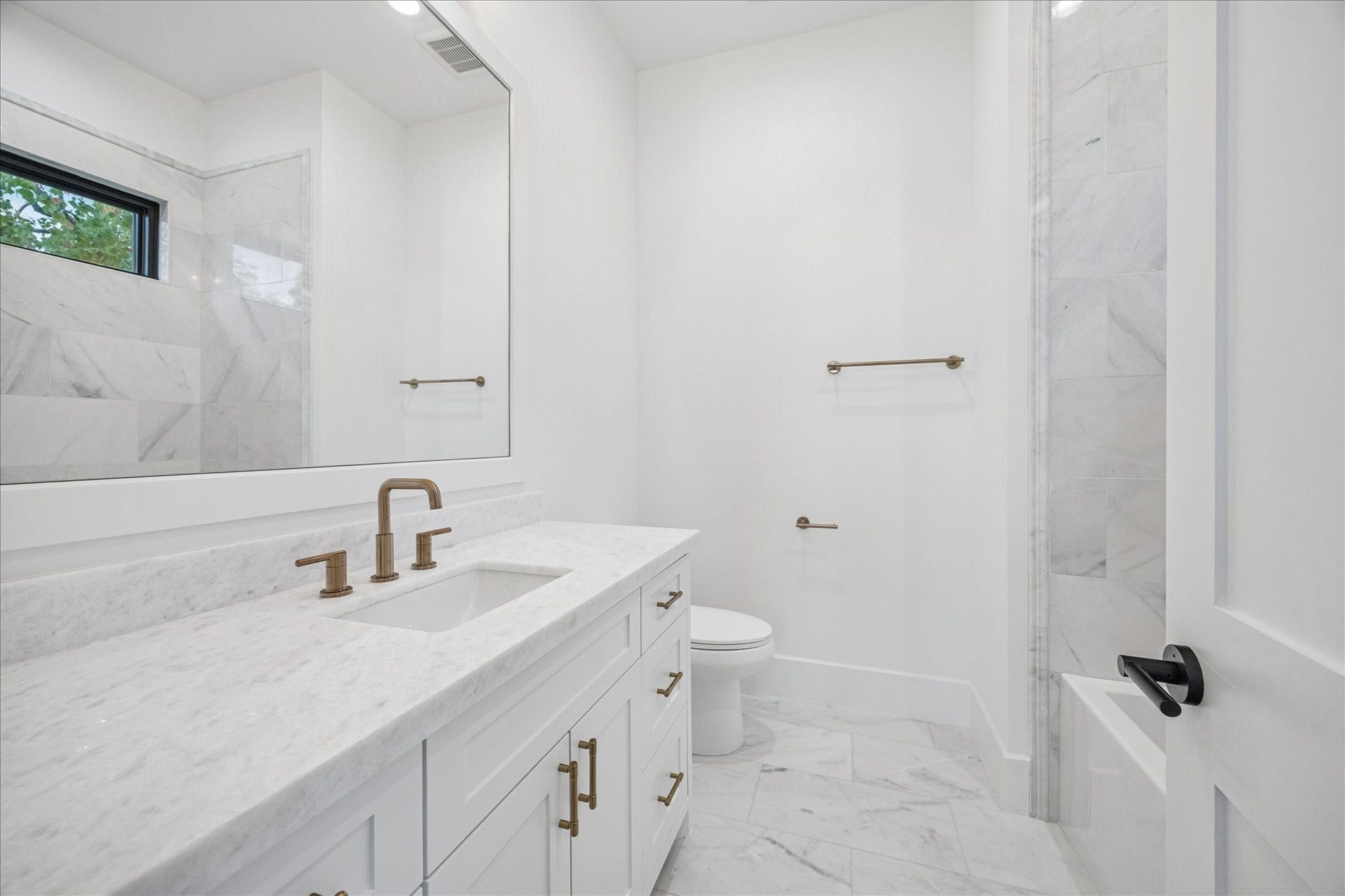 Marble tile climbs the wall while a wide window provides natural light and privacy. Brass fixtures warm the clean palette. *Previous Project*