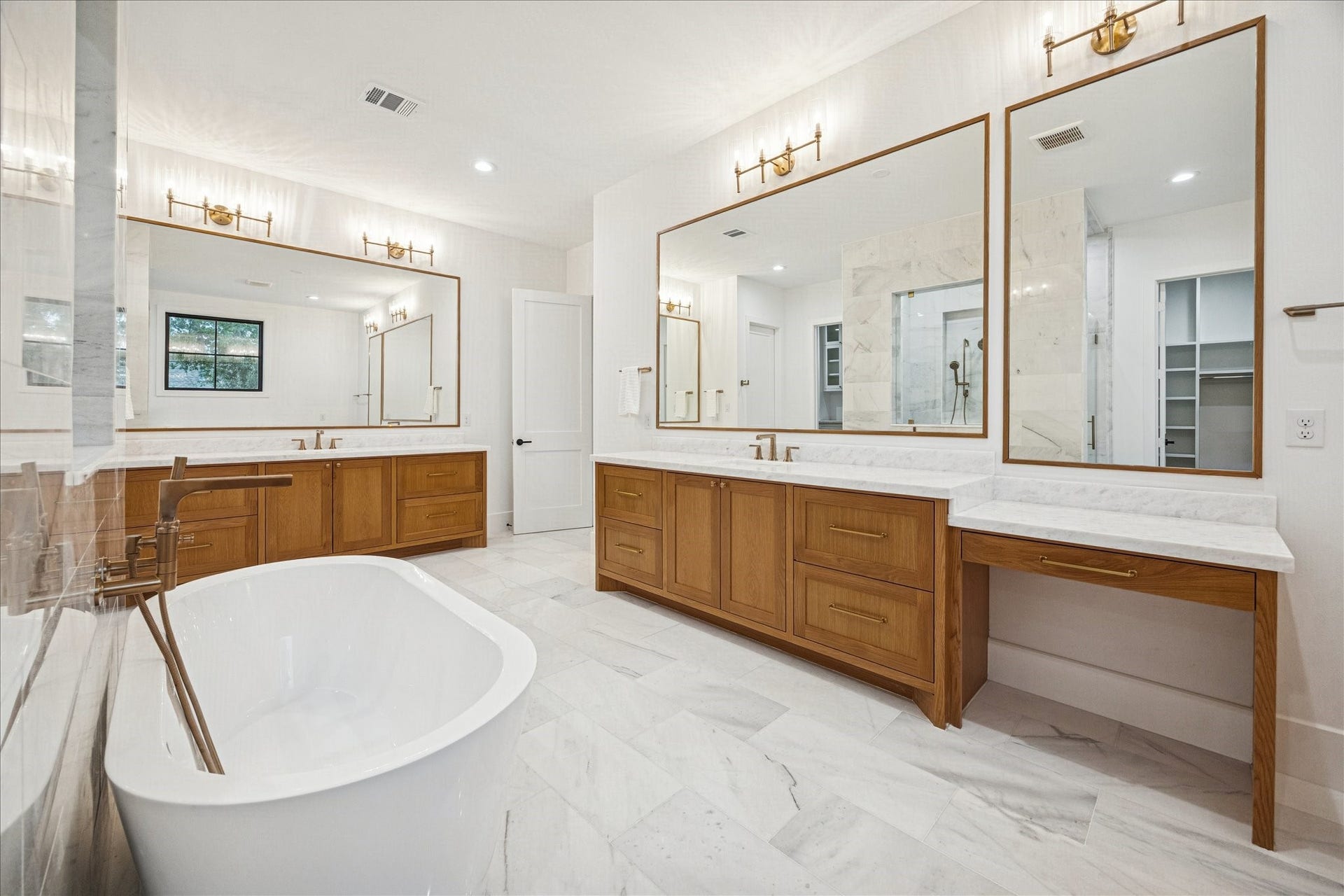 A long marble-topped vanity anchors the suites dressing area, complete with makeup counter, brass lighting, and a built-in beverage fridge. Sunlit windows provide a calming treetop backdrop. *Previous Project*