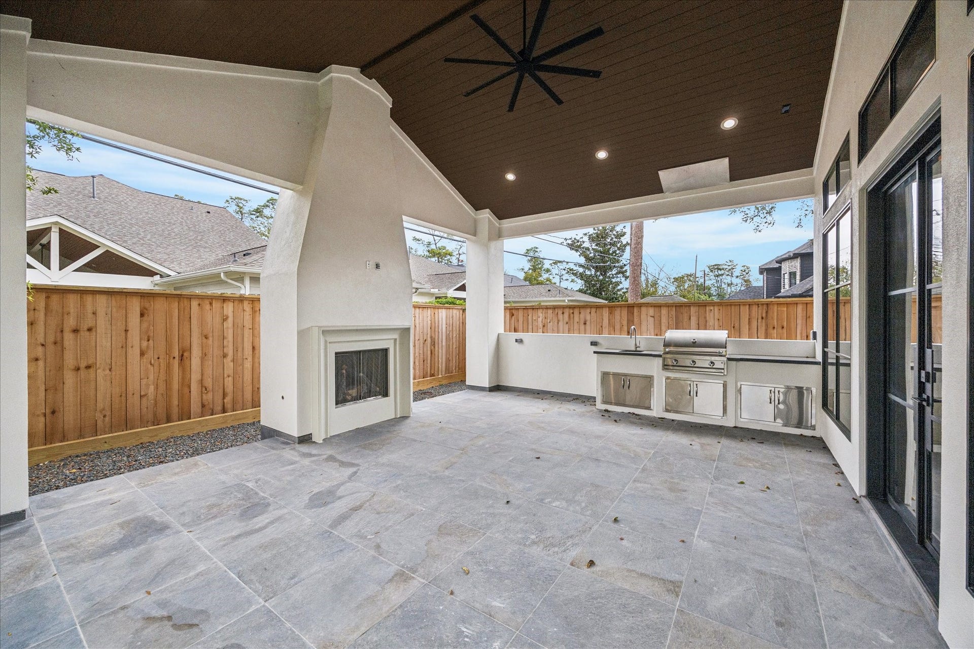 A modern stucco fireplace, V-groove wood ceiling, integrated lighting, and a full summer kitchen  including grill, sink, and storage  create an outdoor retreat crafted for year-round living. *Previous Project*