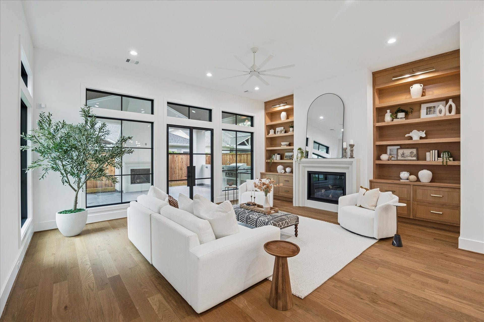 Floor-to-ceiling windows frame views of the covered patio and outdoor fireplace. Custom oak built-ins flank a sleek gas fireplace, adding balance and warmth. The open flow between kitchen, dining, and living creates a cohesive environment for daily living and entertaining. *Previous Project*