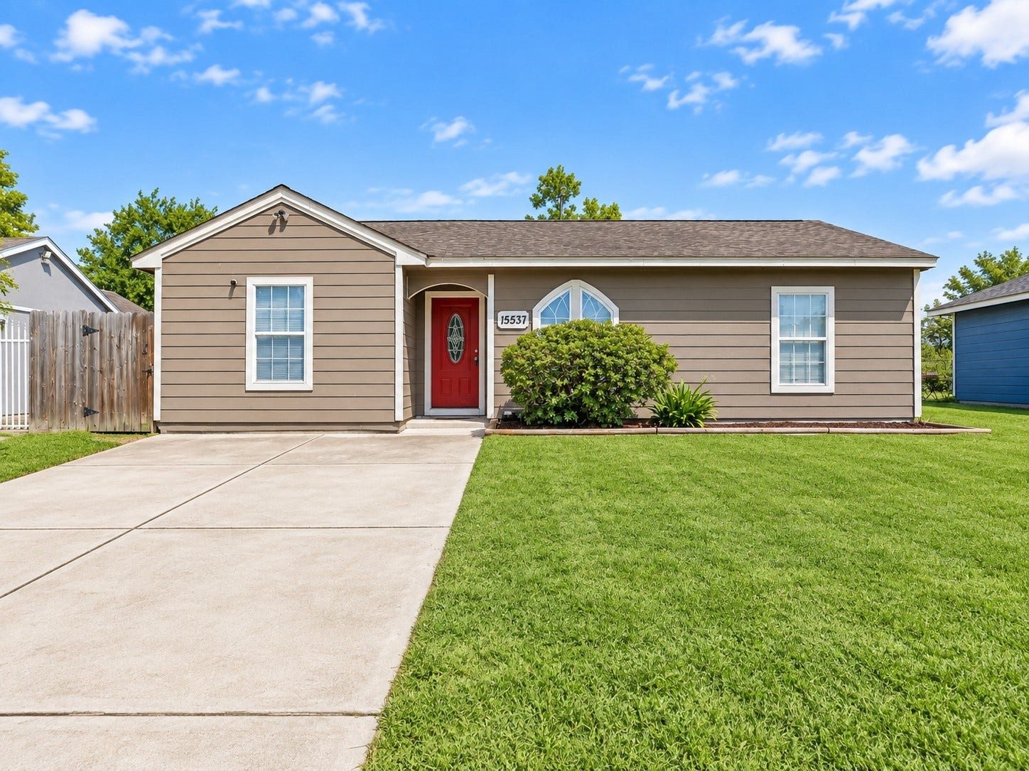 Charming curb appeal welcomes you home with a bold red front door, lush green lawn, and a wide driveway with plenty of parking.