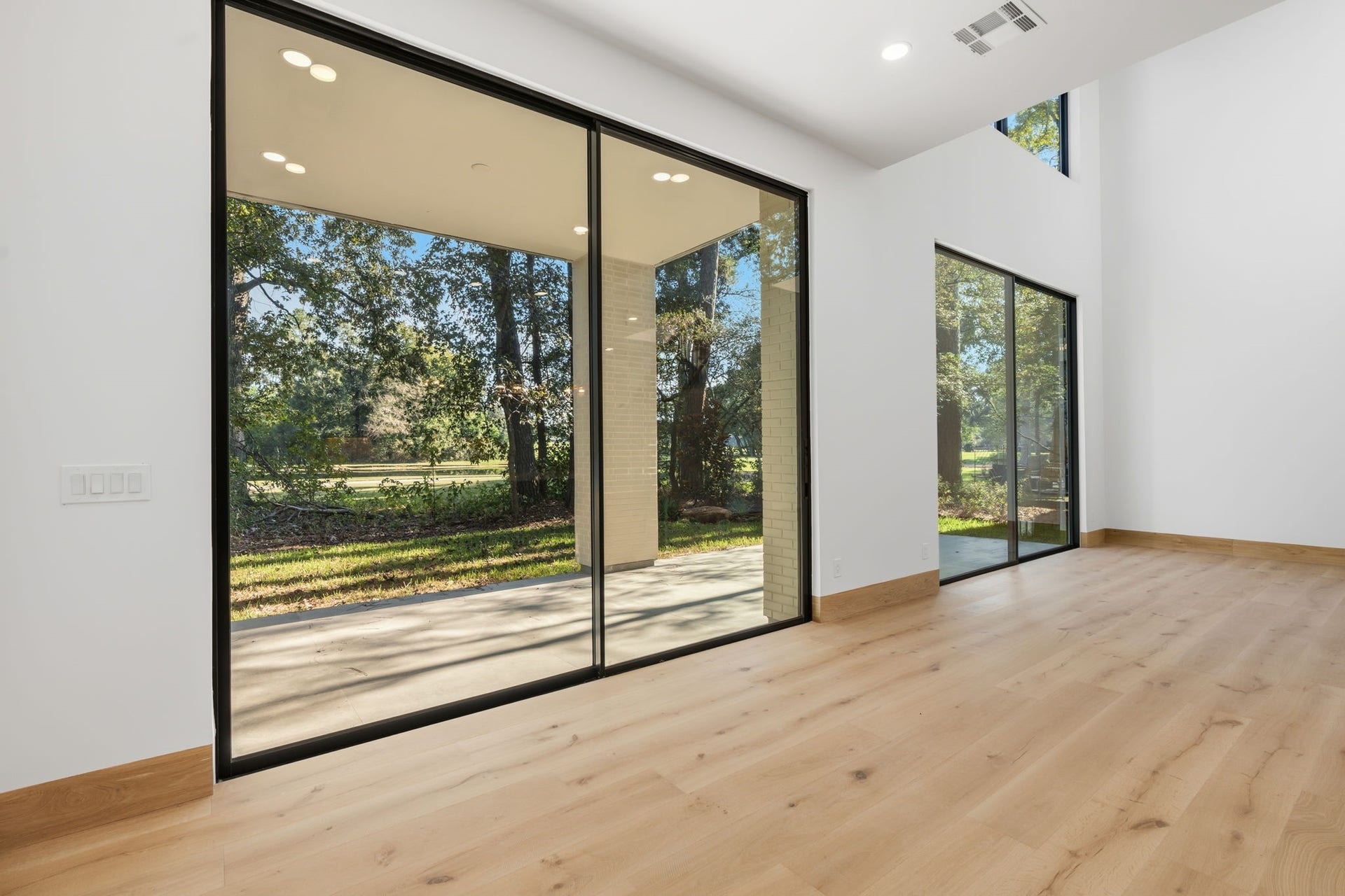 12 N Timber Top Dr, Spring, TX 77380 Sunlit living area boasting soaring double-height ceilings and sliding glass doors that frame picturesque golf course views.