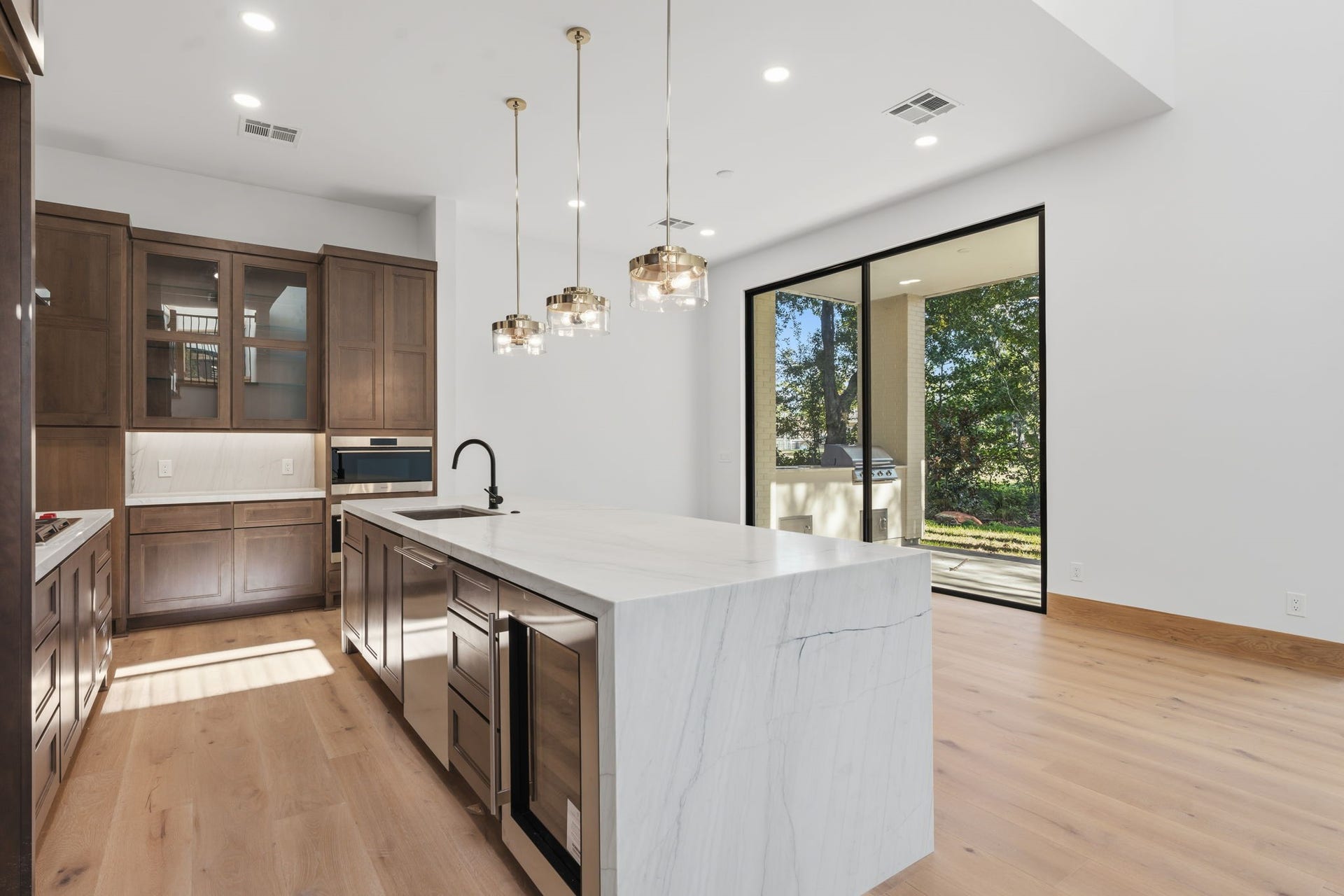 12 N Timber Top Dr, Spring, TX 77380 Gourmet kitchen w/ custom cabinetry, Wolf appliances, waterfall quartz island, beverage fridge & wall-of-glass sliding door to golf course views!