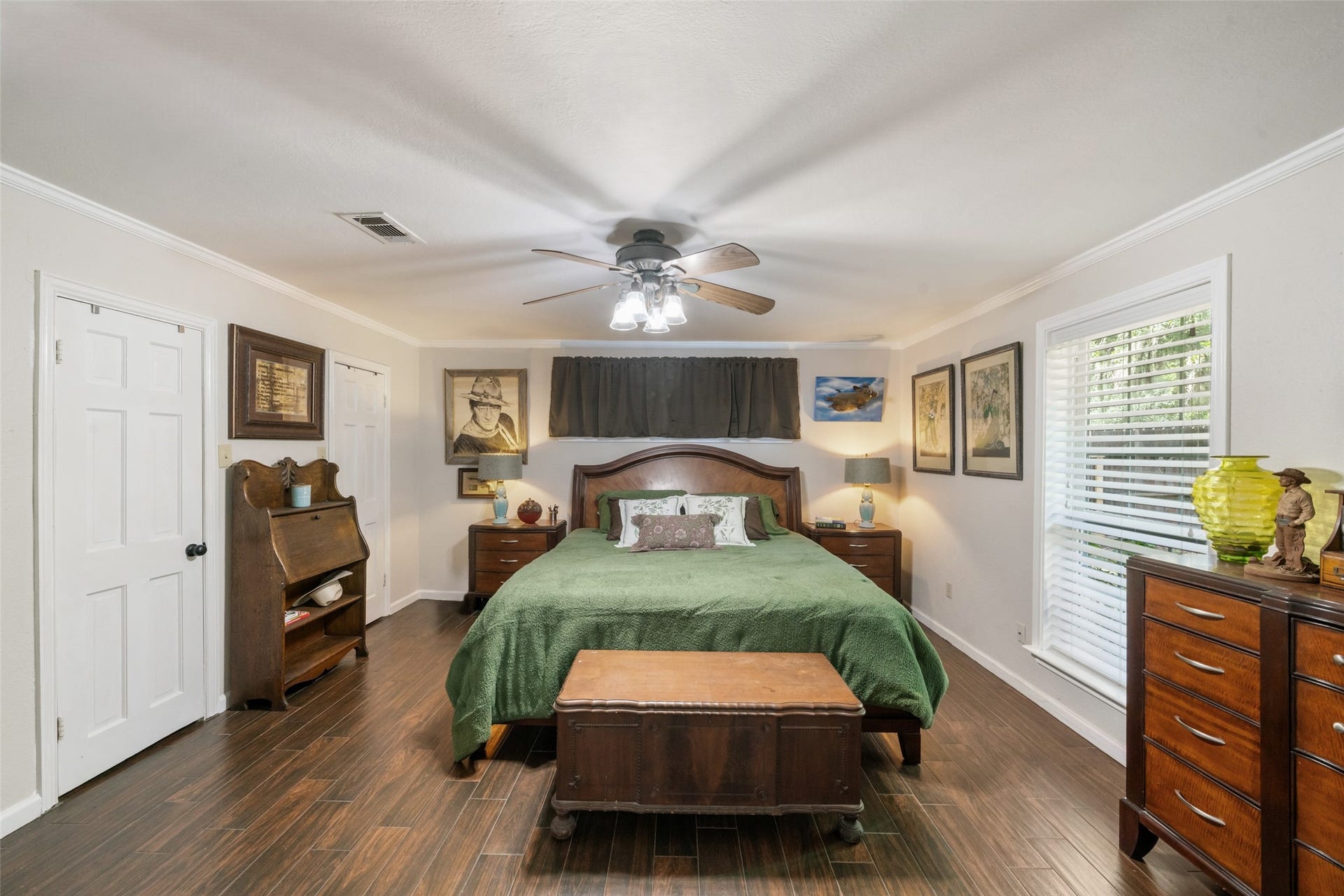 The generously sized primary suite is a calm, beautifully appointed retreat featuring two cedar closets, neutral paint tones, elegant crown molding, and a ceiling fan for year-round comfort. The window offers serene views of the gorgeous hardwoods in the backyard, bringing in natural light creating a relaxing space to unwind. There is also a window positioned above the bed that could be uncovered to introduce even more brightness into the space.