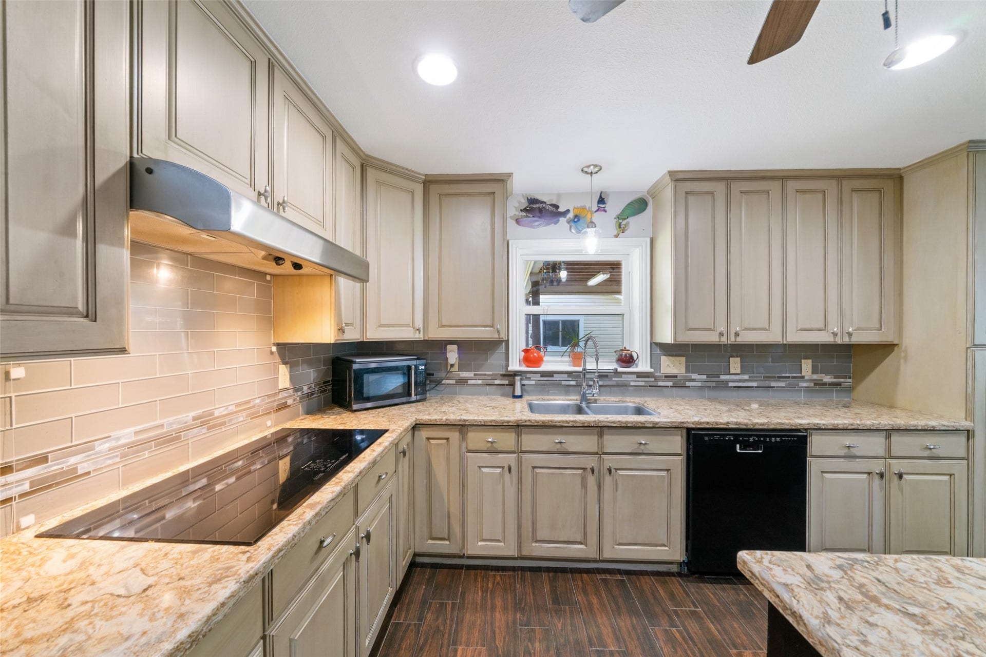 The decorative hardware pulls and stylish backsplash complement the quartz countertop and tile flooring beautifully, creating a cohesive and elevated look throughout the kitchen. A window above the sink provides a pleasant view out to the covered patio, bringing in natural light and adding to the warm, welcoming feel of this kitchen space.