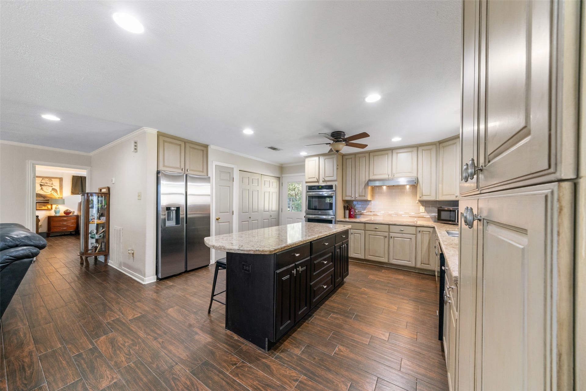 This kitchen features a large island with cabinet space, deep drawers, and even a convenient outlet built right into the island for everyday use. The stunning wood-look tile plank flooring runs throughout the home, adding warmth and durability. Recessed lighting brightens the entire space, and with the primary bedroom just a few steps away, those late-night snack runs couldnt be easier.