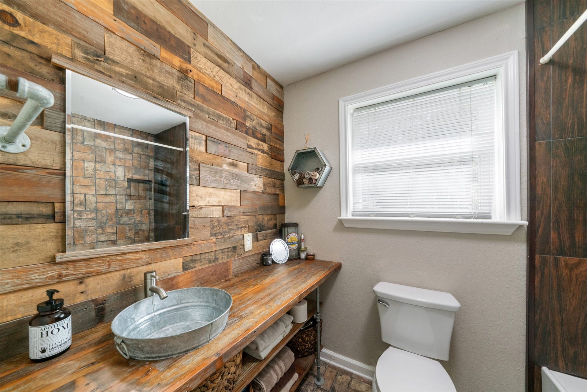 The secondary bath is truly charming, featuring a window that brings in soft natural light and highlights the beautiful accent wall that adds warmth, texture, and a unique rustic touch. The standout feature is the one-of-a-kind vanity with its galvanized basin sink and wood-style countertop, giving the space a custom, farmhouse feel that sets it apart. Its a thoughtfully designed area that blends character with functionality. The brick style floor tile is absolutely gorgeous in this space.