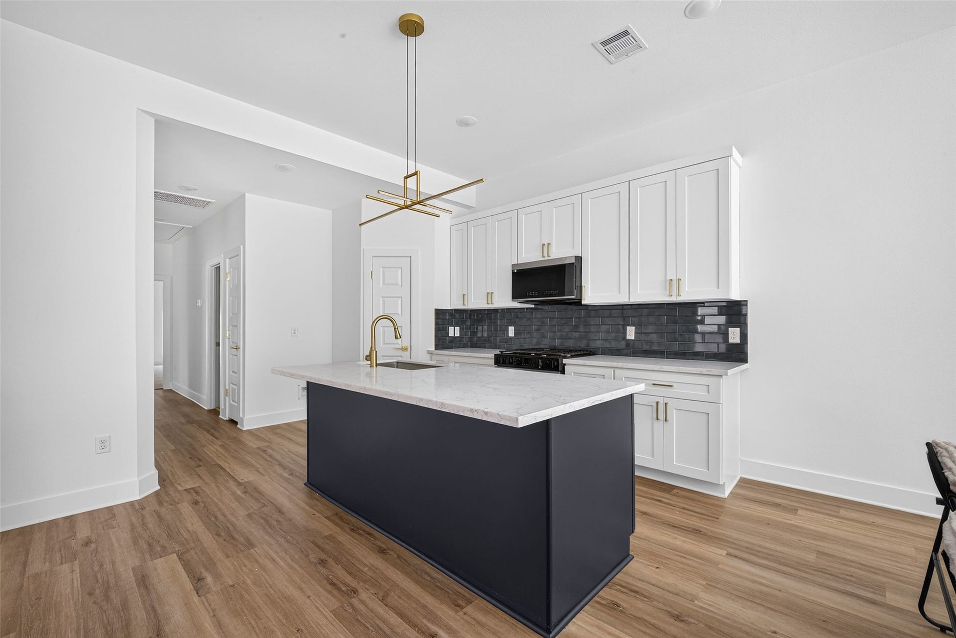 9309 Caddo Road, #A/B, Houston, TX 77078 Photo 2 (Kitchen Island Detail):
A true centerpiece of the home. Elegant designer pendant lighting hangs above a stylish central island, illuminating crisp white cabinets and a high-contrast dark backsplash set against warm flooring.