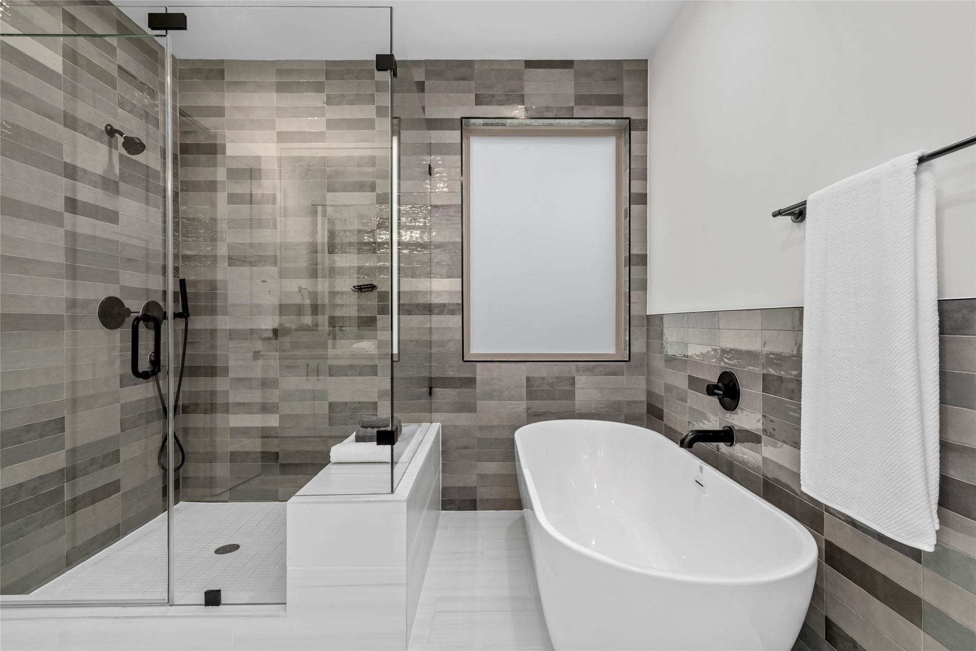 2410 Elmen Street, Houston, TX 77019 Full walls of tile surround this frameless glass enclosed shower with hand shower, contrast floor tile and a shower seat. Floor tile is porcelain. Another custom shade on the window over the tub.