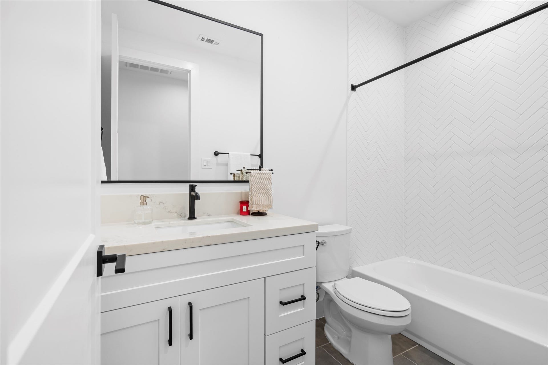 2410 Elmen Street, Houston, TX 77019 Bathroom shared by bedroom two and three. Quartz counter top, tile, matte black hardware and bathroom fixtures. Metal framed mirror, porcelain floor tile and herringbone ceramic tile in tub/shower.