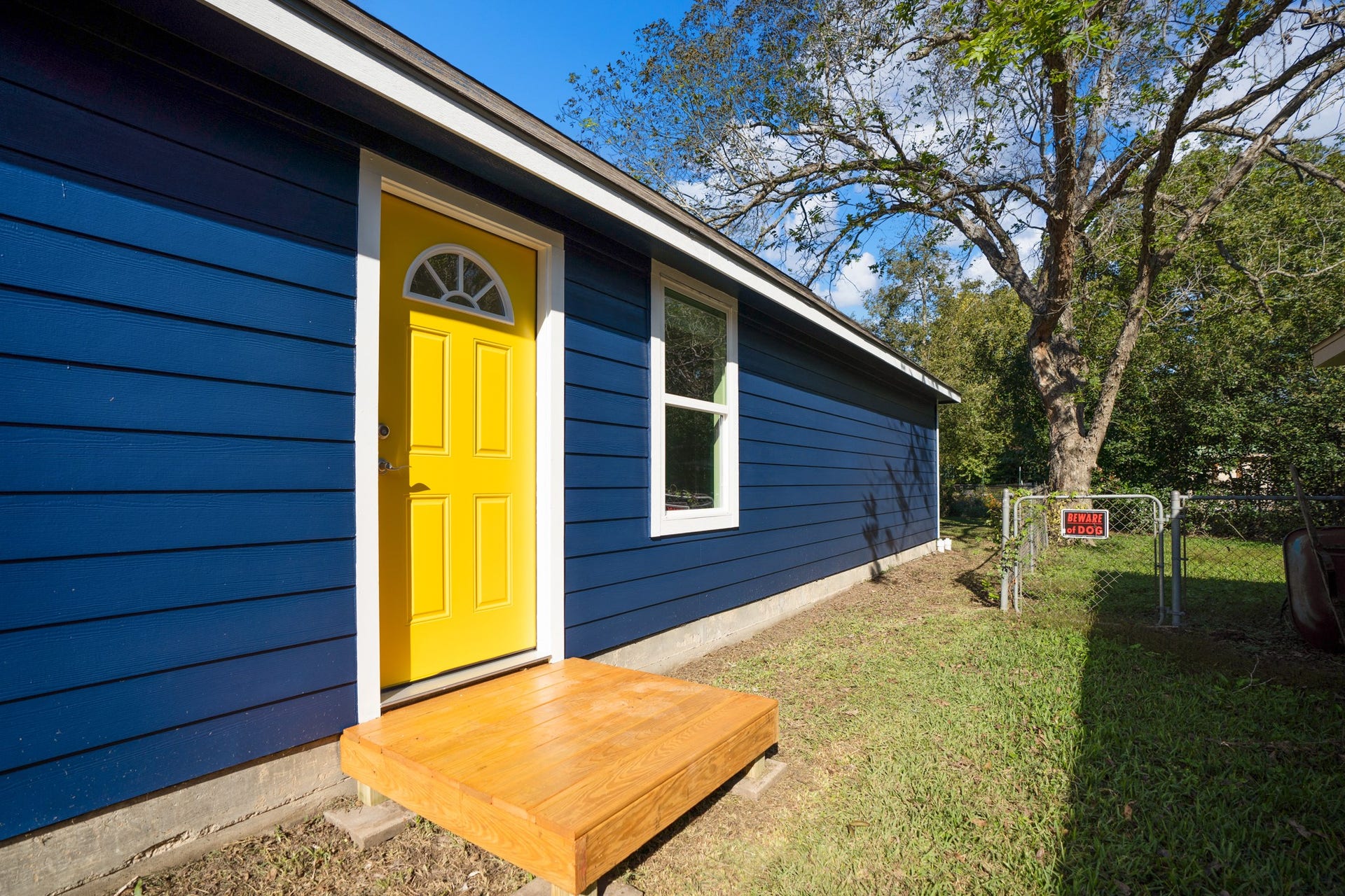 306 Foster Street, Tomball, TX 77375 Another pop of yellow! This side entrance opens into the hallway between the main living area & bedrooms, offering another convenient way in and out of the home. A wooden landing leads to the grassy side yard, with gated access just beyond.