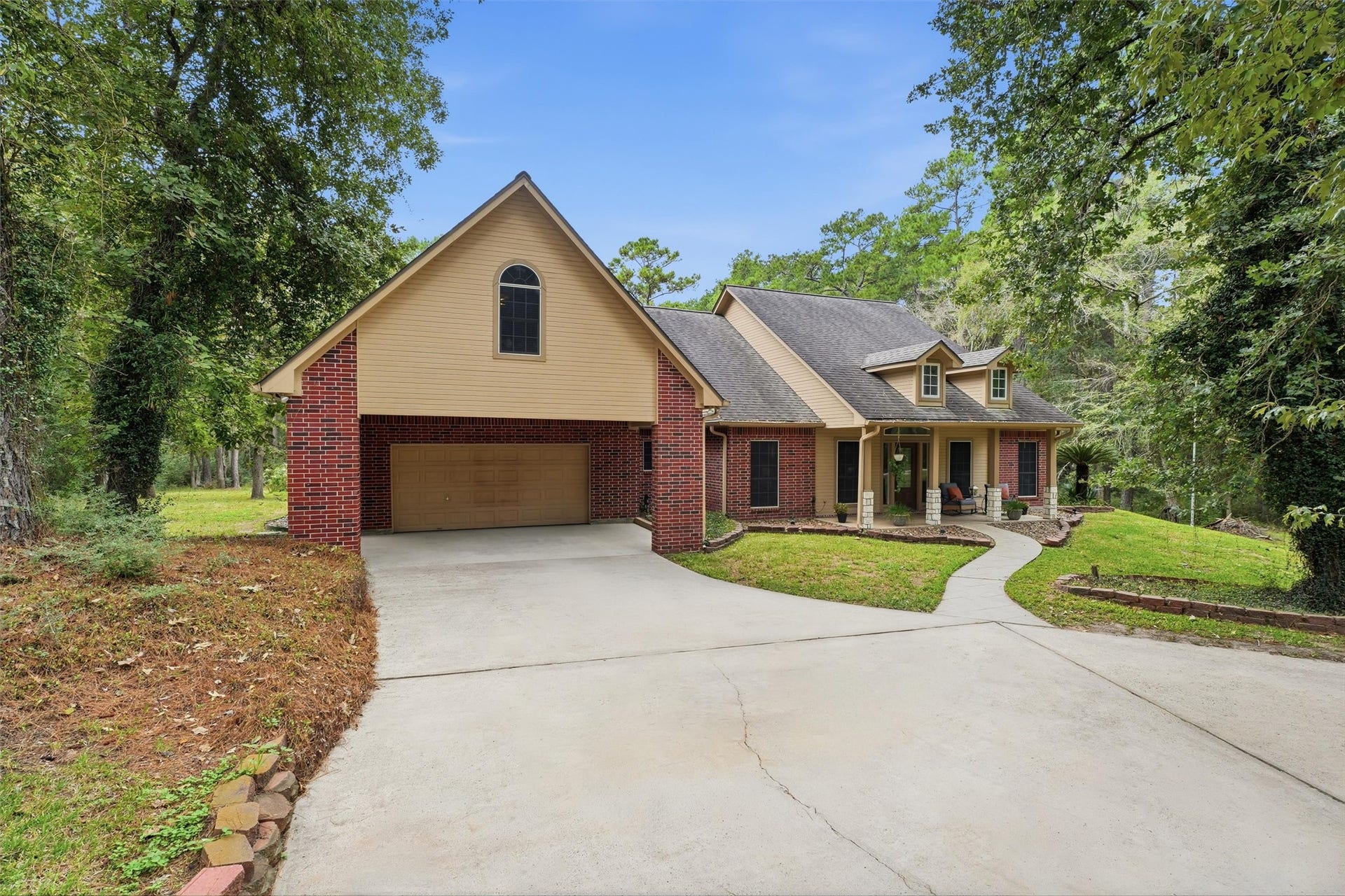 Charming 1.5 story home with a classic brick exterior, nestled among mature trees. Features a spacious driveway leading to a two-car garage and a welcoming front porch.