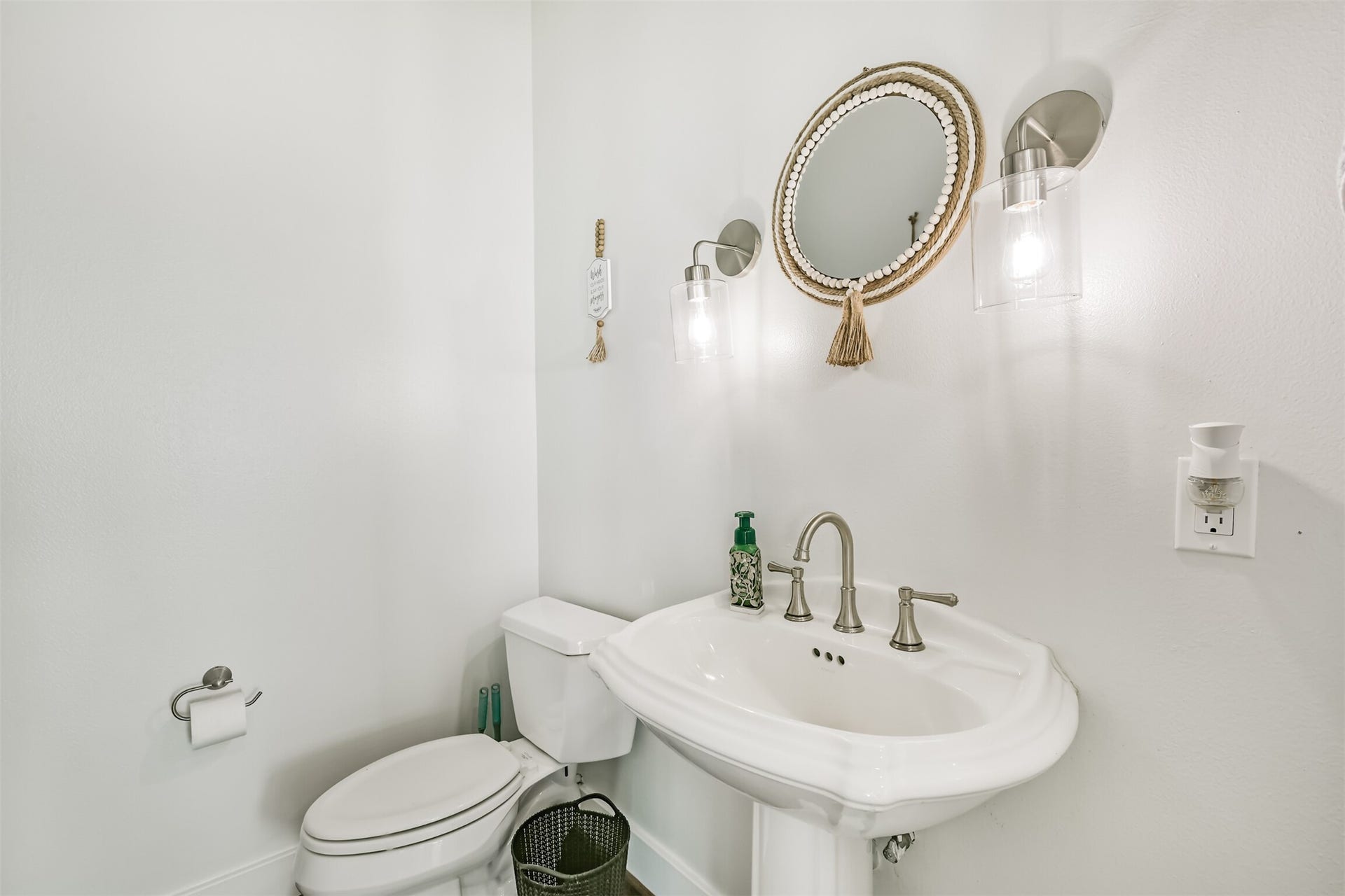 Powder room featuring a classic pedestal sink, elegant wall sconces, and a decorative round mirror.