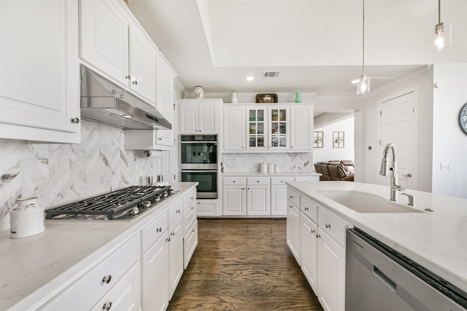 Elegant kitchen featuring modern white cabinetry, a sleek marble backsplash, and a spacious island with a built-in sink and dishwasher.