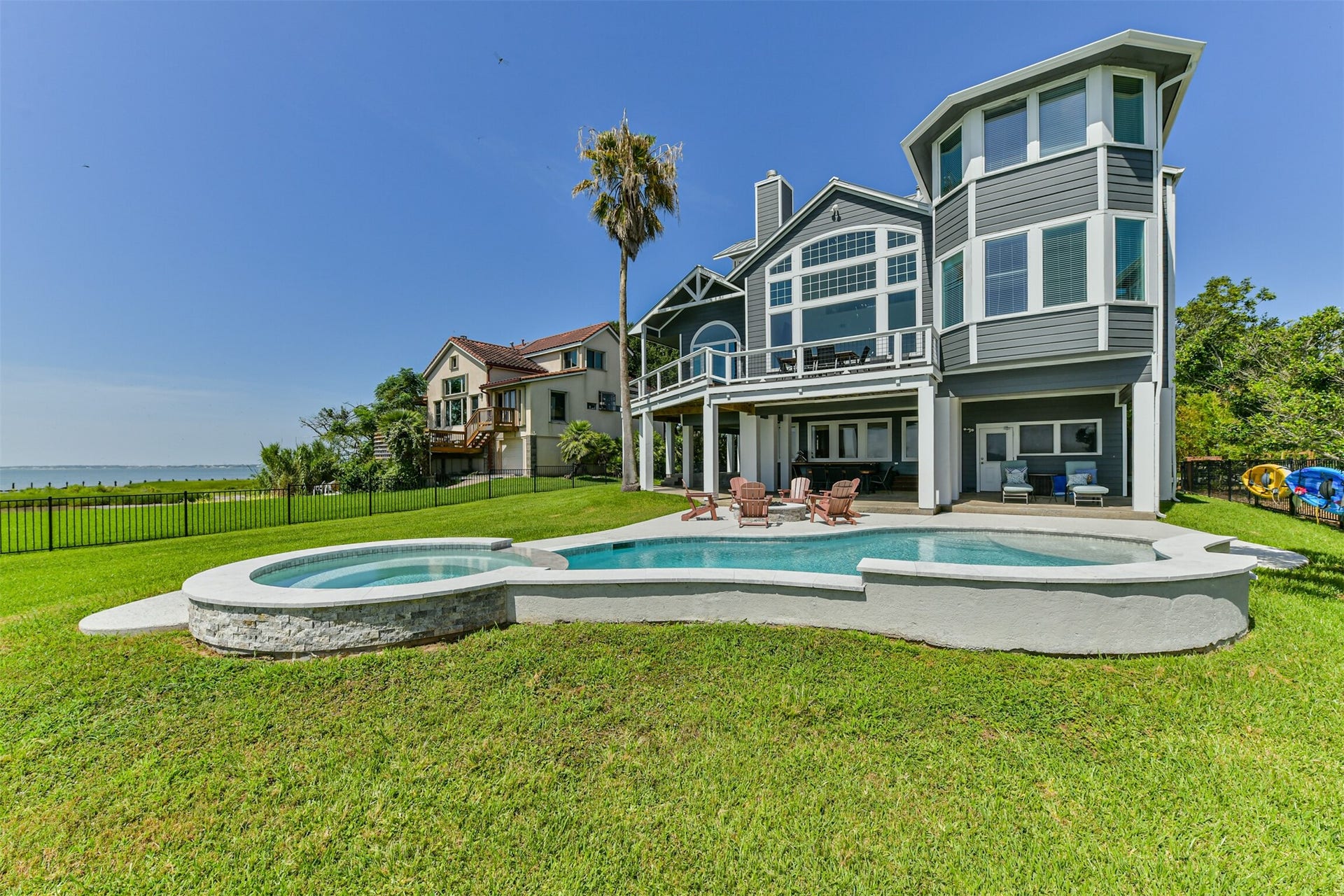Stunning waterfront home with expansive windows and a spacious patio overlooking a sparkling pool, perfect for relaxation and entertaining.