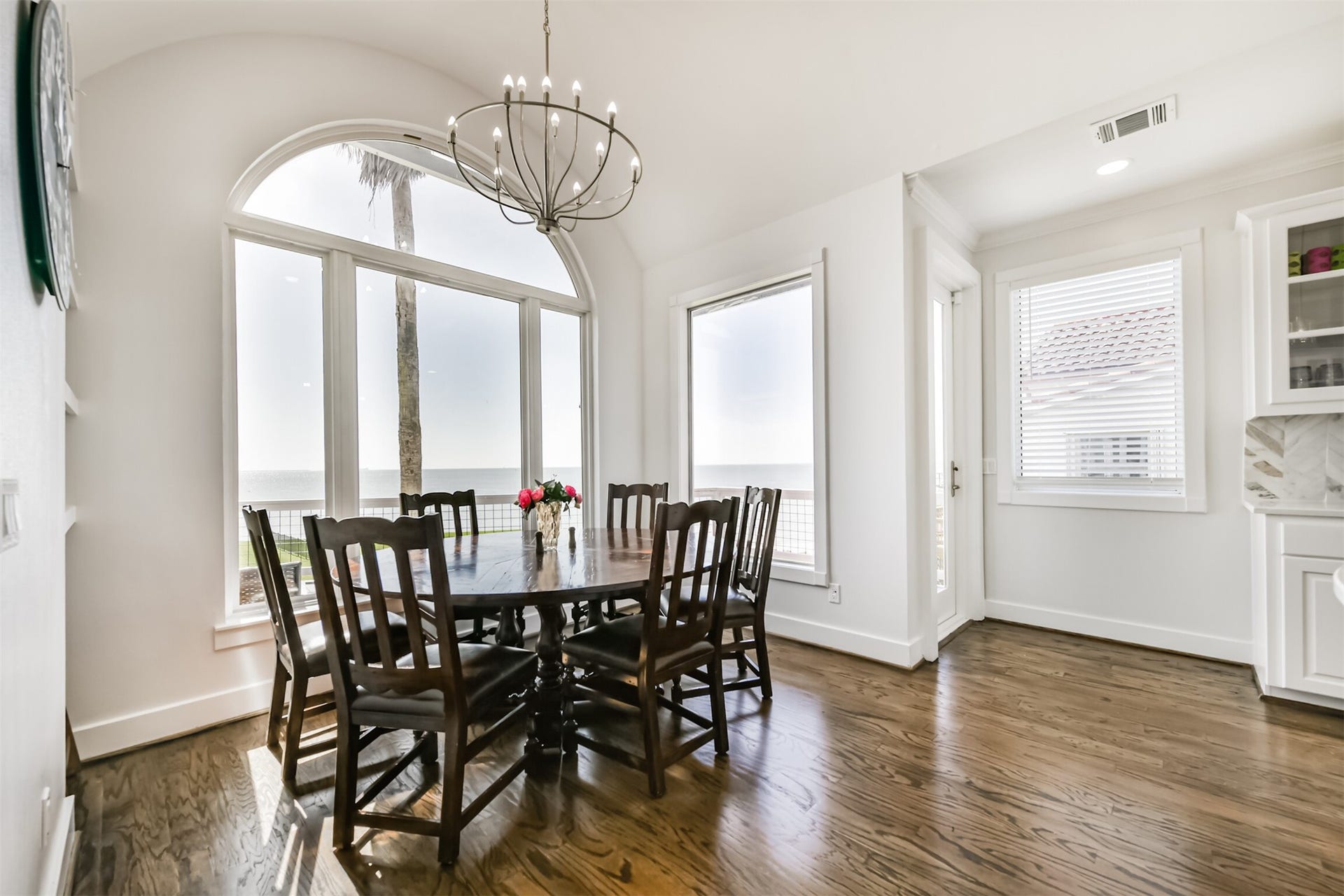 Dining area with stunning ocean views through large arched windows, featuring elegant wood flooring and a stylish chandelier.