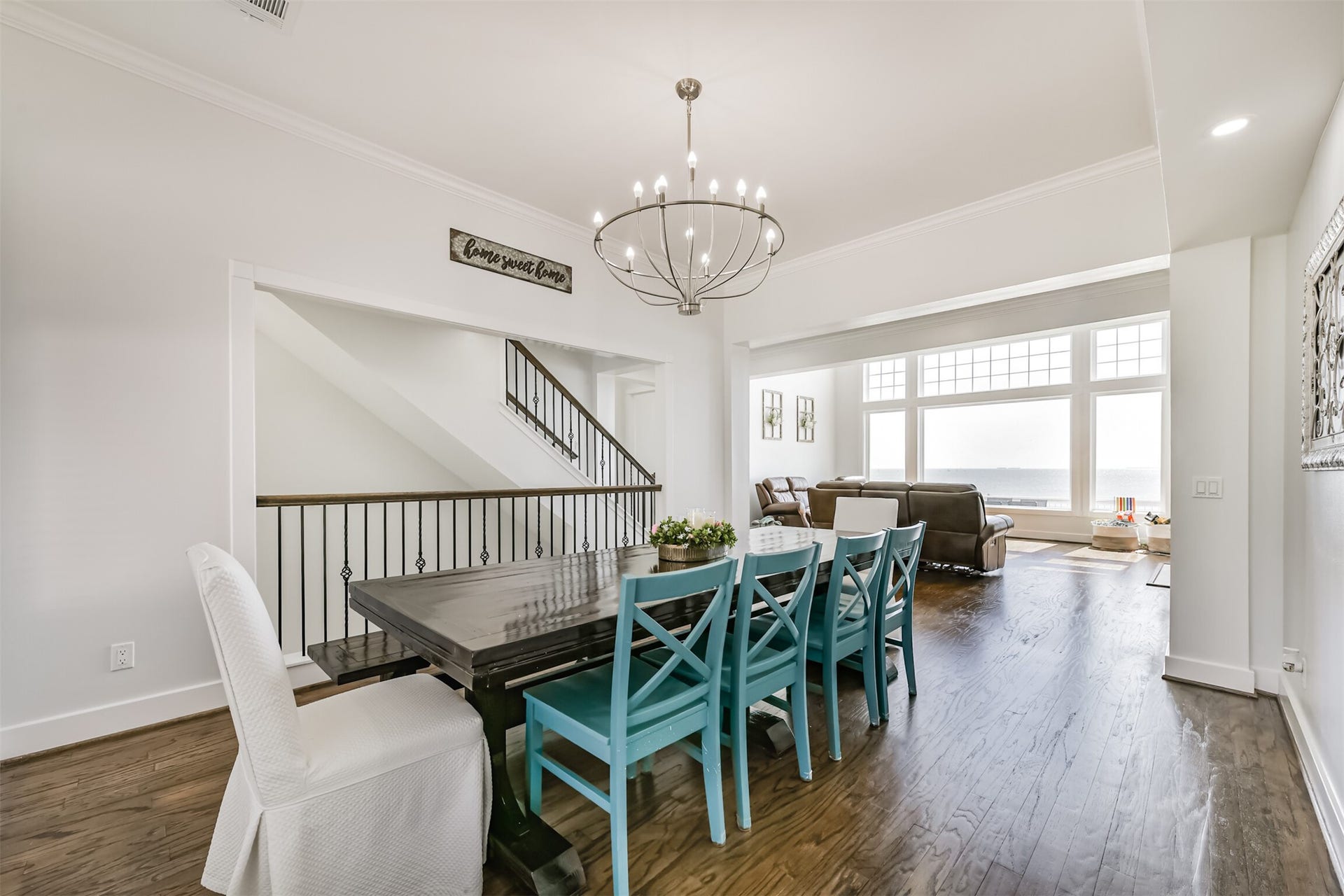 Dining area with a modern chandelier, featuring a spacious table and vibrant chairs, seamlessly flowing into a cozy living room with expansive windows offering stunning views.