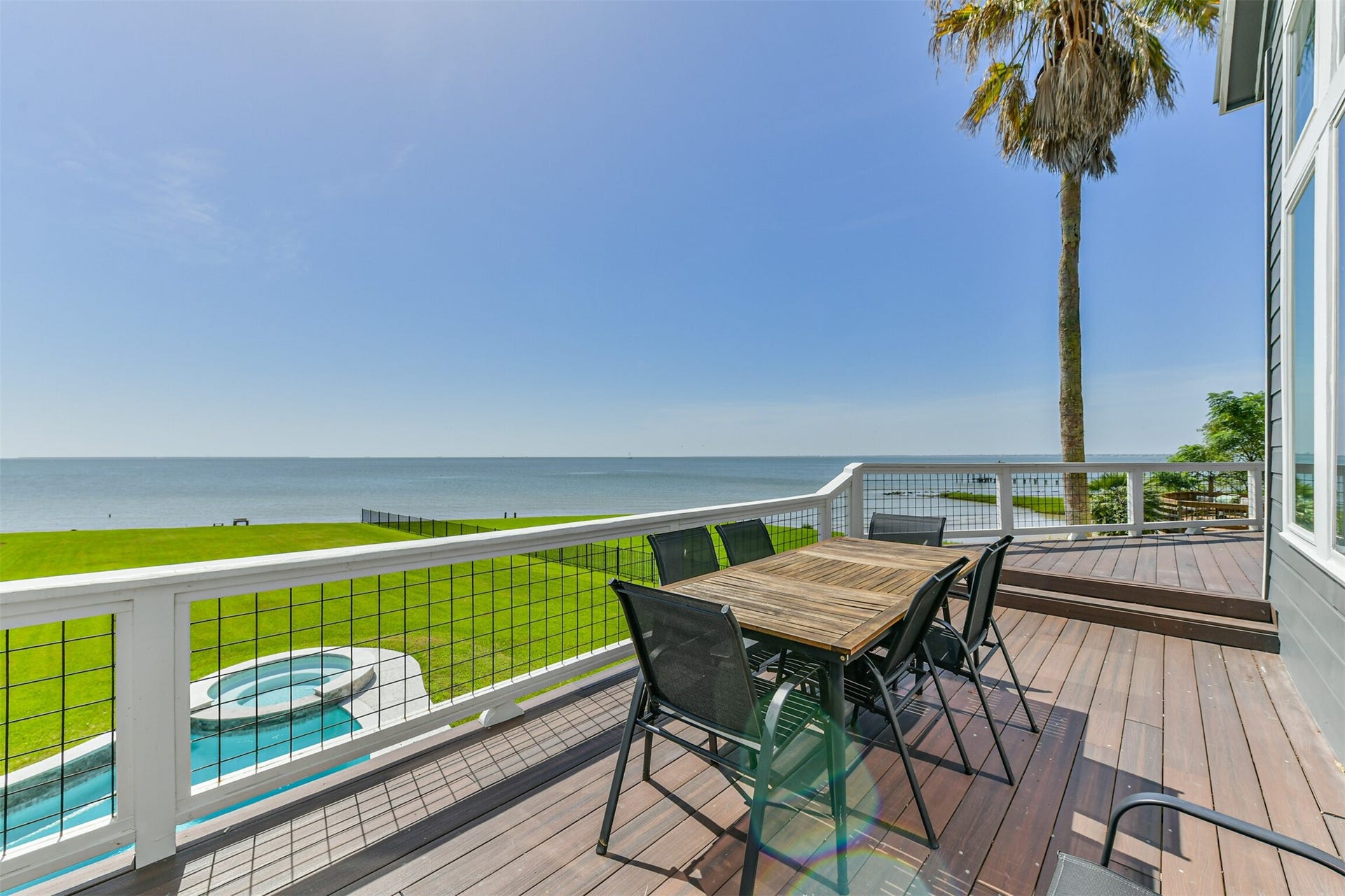 Stunning oceanfront deck with panoramic views, perfect for outdoor dining and relaxation, overlooking a lush lawn and inviting pool.