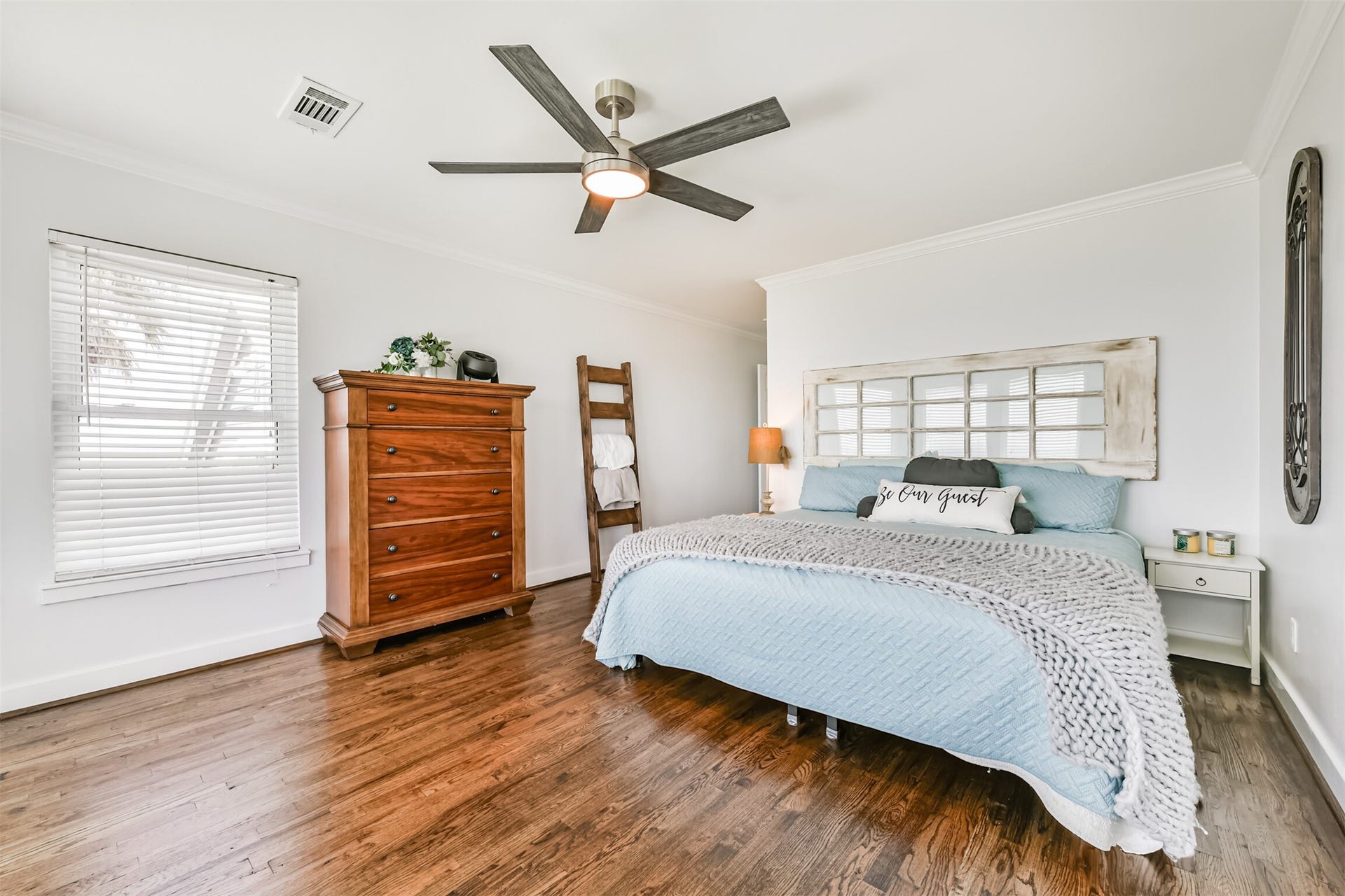 Bedroom featuring gleaming hardwood floors, a stylish ceiling fan, and abundant natural light. Cozy decor and neutral tones create a welcoming ambiance.
