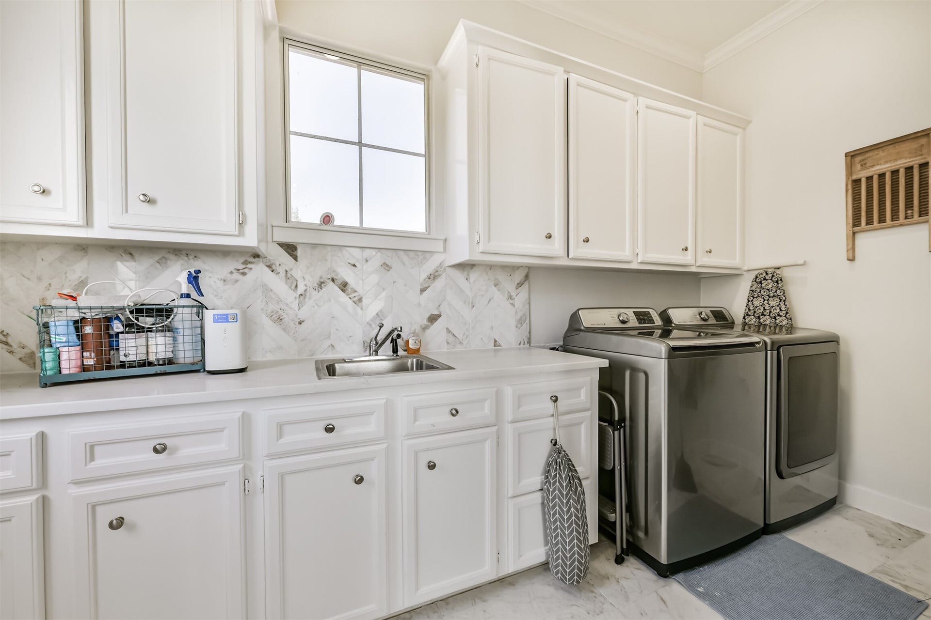 Laundry room featuring ample cabinetry, modern appliances, and a stylish herringbone backsplash.