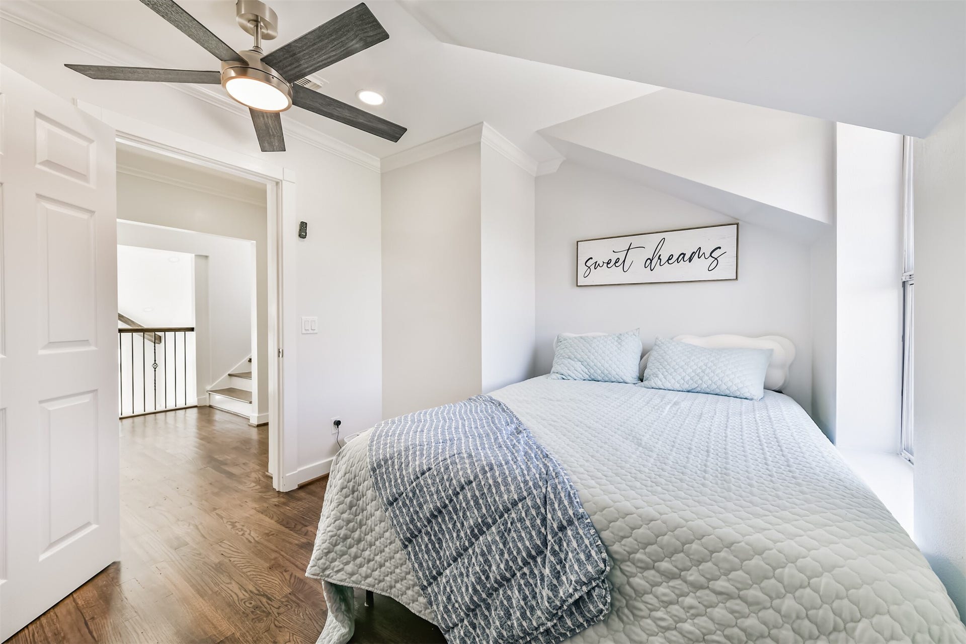 Charming bedroom with a cozy bed under a sloped ceiling, featuring soft lighting and a ceiling fan for comfort.