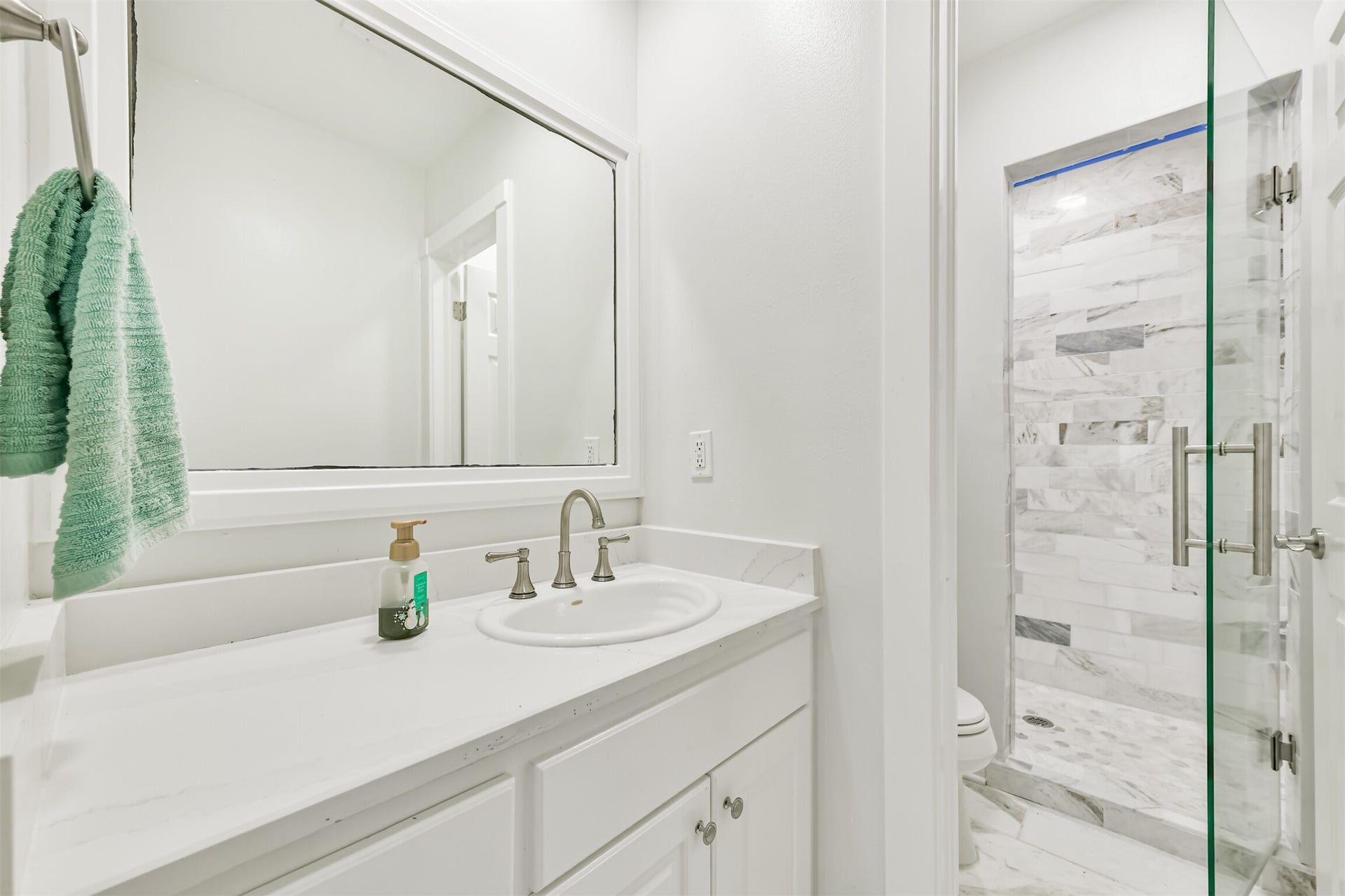 Bathroom featuring a sleek vanity with a large mirror, complemented by a glass-enclosed shower with elegant tile work.