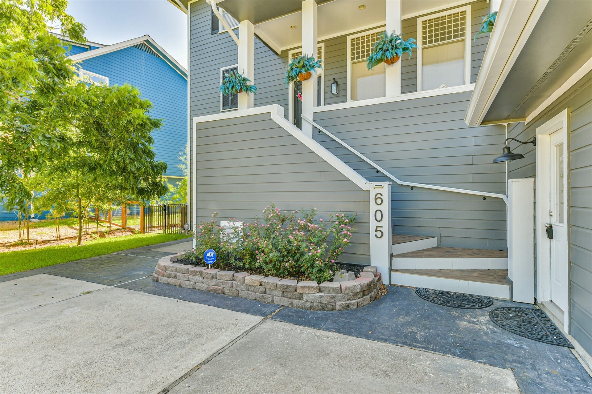 Entryway with a welcoming staircase, accented by vibrant planters and neatly landscaped garden beds, leading to a stylish gray exterior.