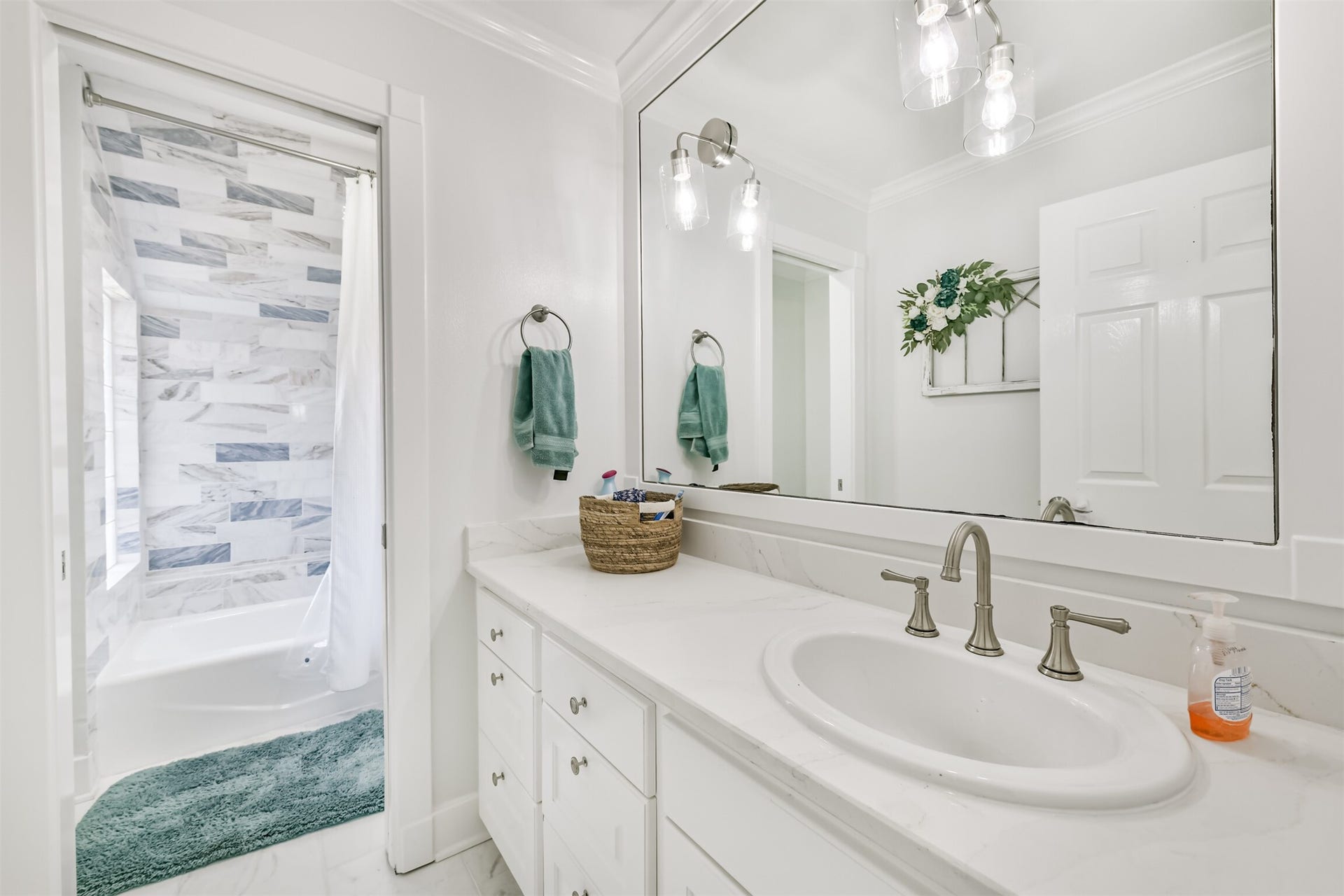 Bathroom featuring a sleek vanity with dual faucets, a large mirror, and a modern shower with elegant tile work.