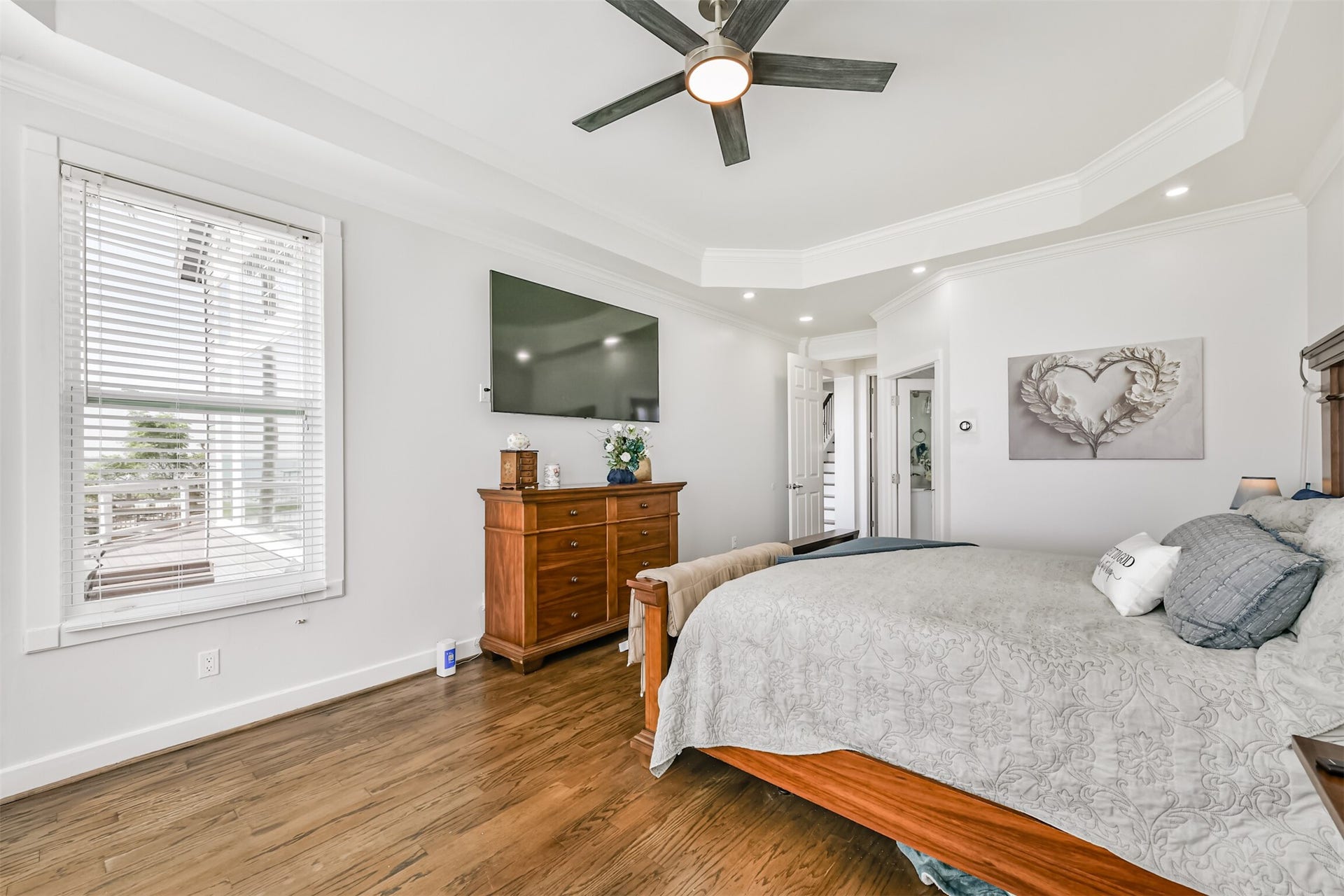 Bedroom with elegant tray ceiling, hardwood floors, and abundant natural light.