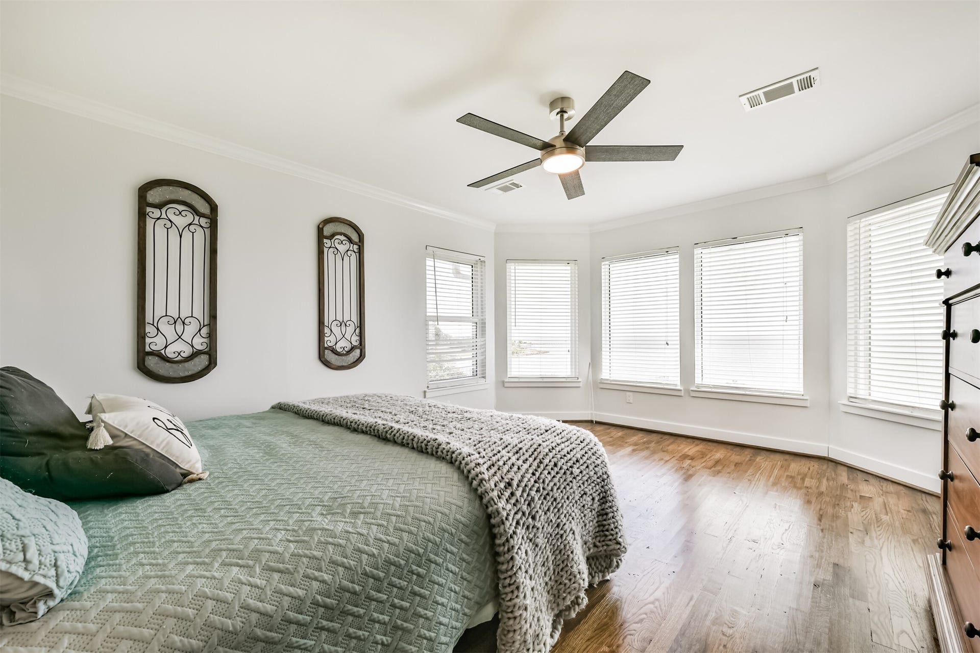 Bedroom with abundant natural light streaming through multiple windows, featuring elegant hardwood floors and a modern ceiling fan.