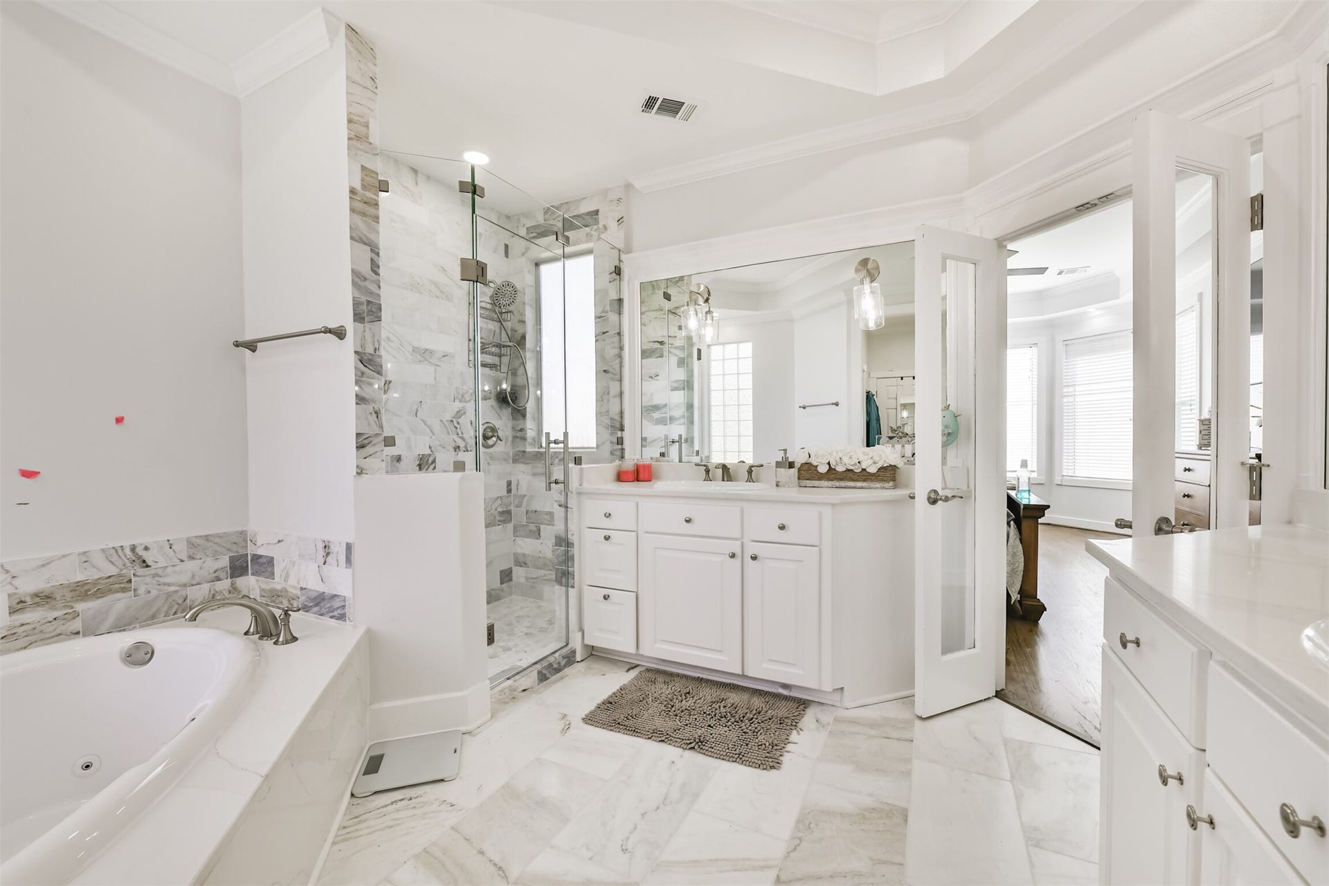 Luxurious bathroom featuring elegant marble flooring, a spacious glass-enclosed shower, and a relaxing whirlpool tub, complemented by double vanities and ample natural light.