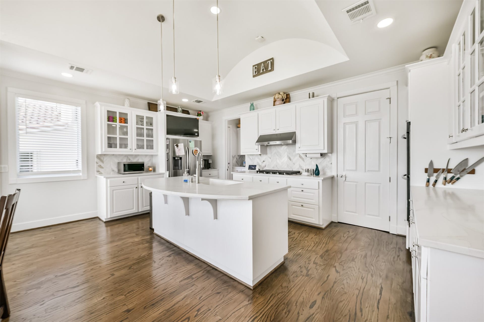 Bright kitchen with elegant white cabinetry, a central island, stainless steel appliances, and hardwood floors, creating a modern and inviting space.