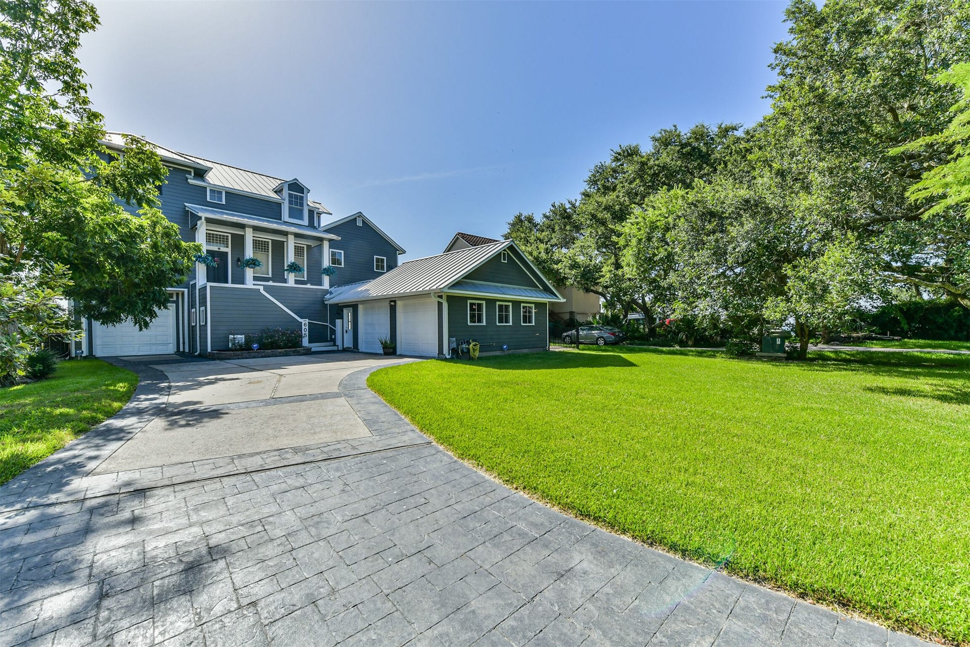 Stunning home with elegant gray siding, a spacious driveway, and beautifully landscaped front yard surrounded by lush trees, offering both elegance and tranquility.