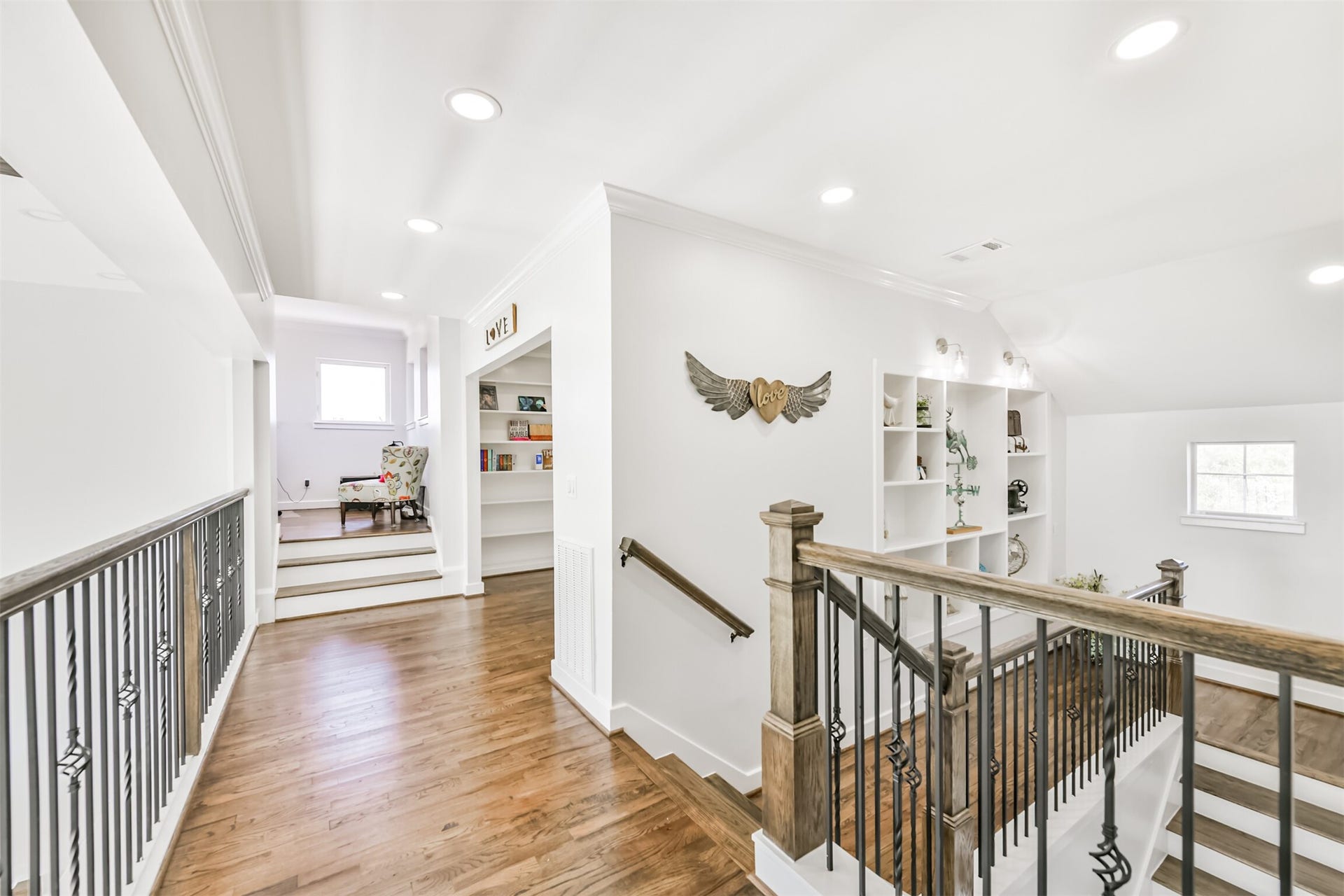 Bright and inviting upper-level landing with elegant wood flooring, built-in shelving for display, and decorative accents. The space is complemented by stylish railings and leads to a cozy reading nook.