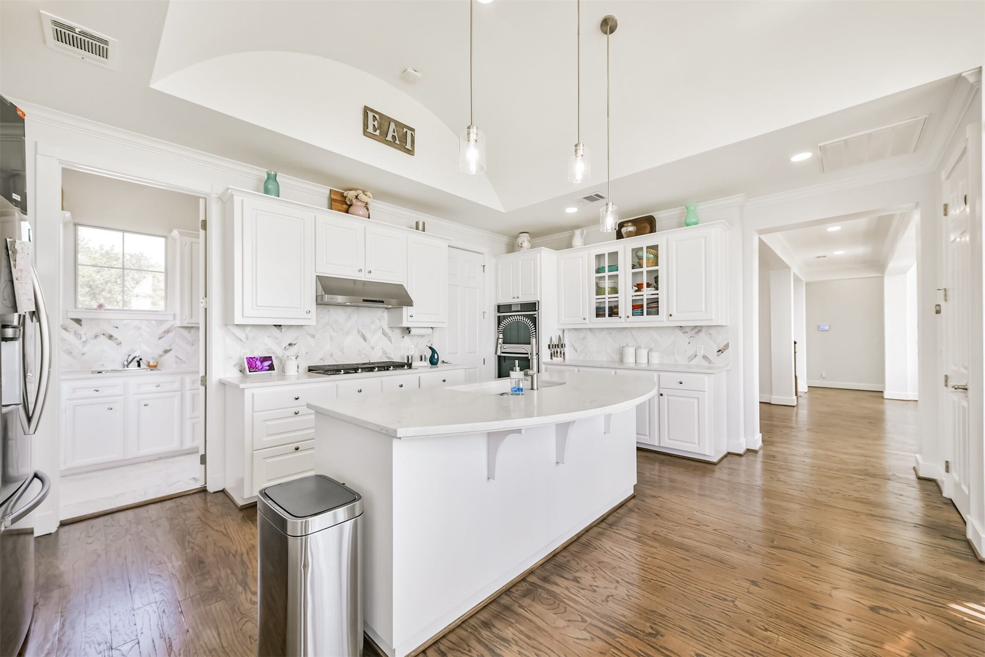 Spacious kitchen featuring elegant white cabinetry, a large central island with pendant lighting, and sleek stainless steel appliances, all enhanced by beautiful hardwood flooring.