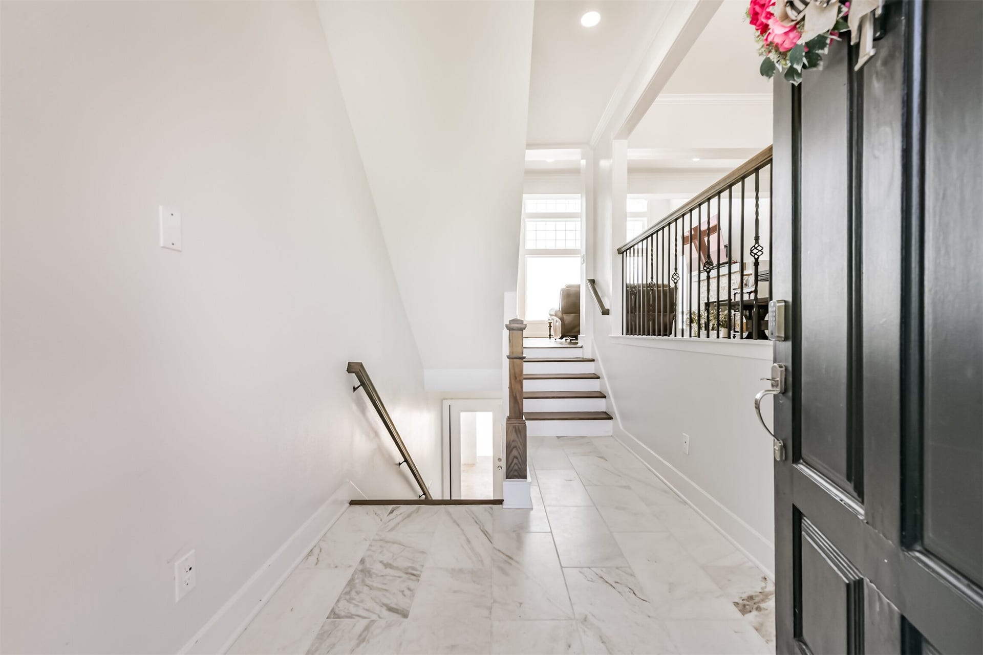 Inviting entryway featuring elegant marble flooring and a stylish open staircase leading to a sunlit living area.