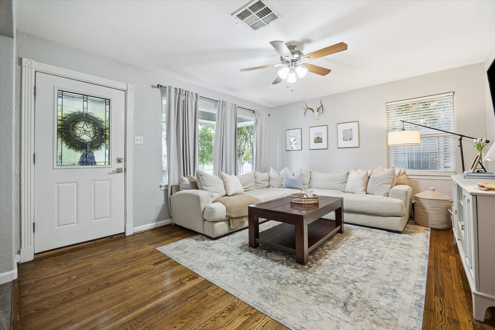 Second view of the living room is bright and comfortable with hardwood floors, large windows, and a ceiling fan for year-round comfort.