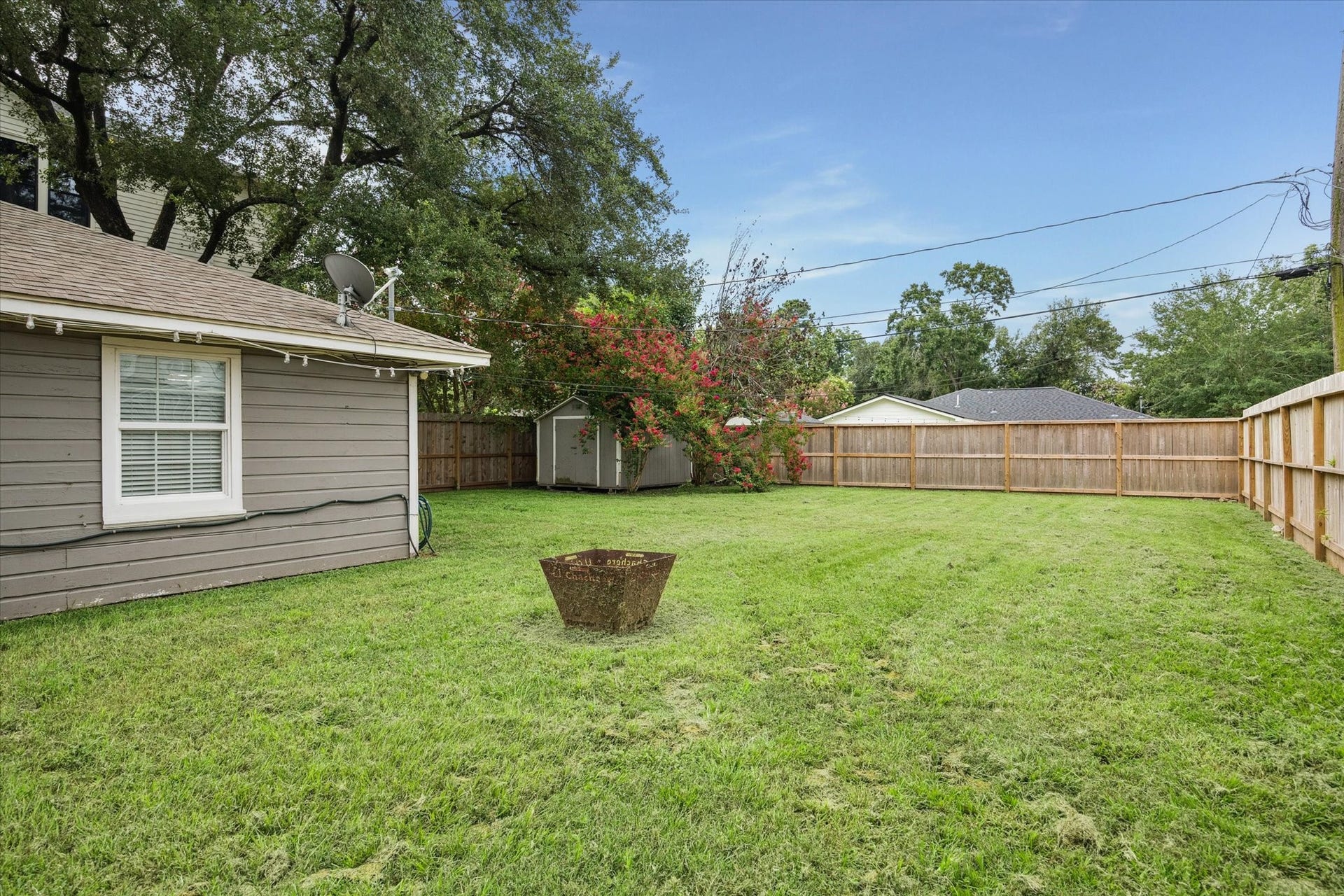 The fully fenced backyard offers a wide open lawn with mature trees along the perimeter and a dedicated firepit area.