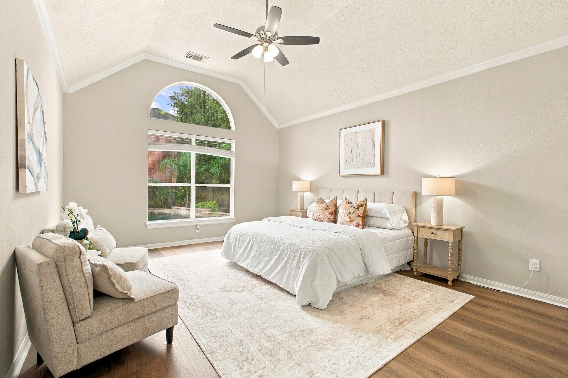 Primary bedroom featuring vaulted ceilings, wood flooring, and a large arched window overlooking the backyard.