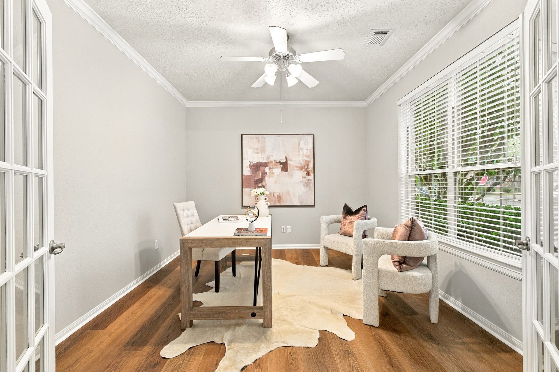 Private home office featuring French doors, wood flooring, and a large window offering abundant natural light and street views.