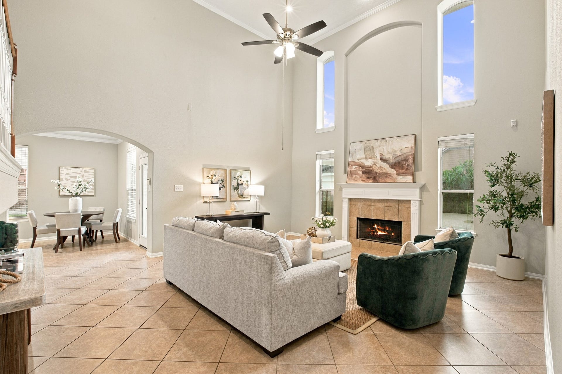 The spacious living room features soaring ceilings, an elegant fireplace, abundant natural light, and an open layout that flows seamlessly into the dining area.