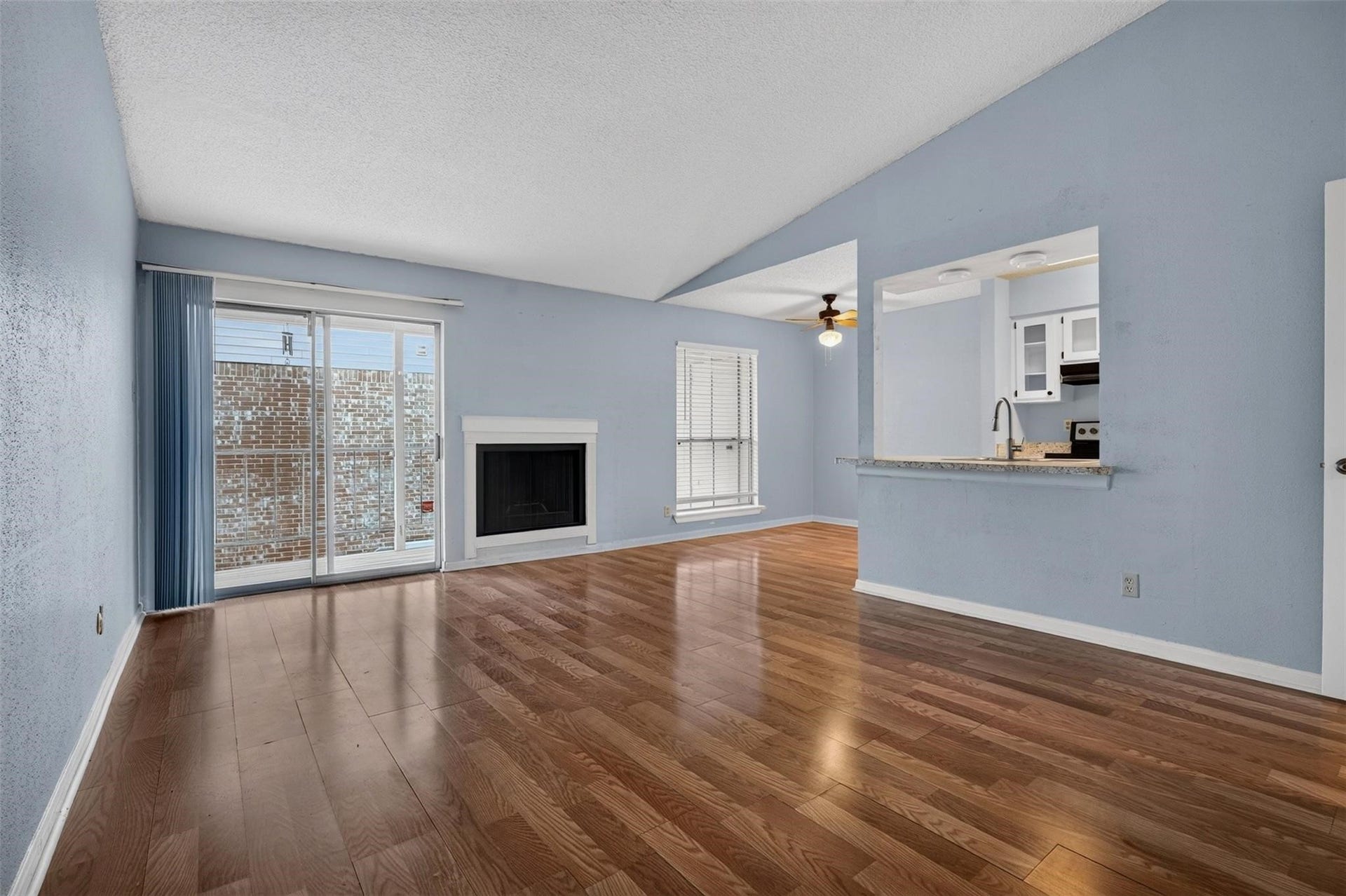 700 Thicket Lane, #304, Houston, TX 77079 Spacious living area with warm wood flooring, featuring a cozy fireplace and abundant natural light from large sliding glass doors. The open layout seamlessly connects to a modern kitchen with a convenient passthrough and stainless steel appliances.