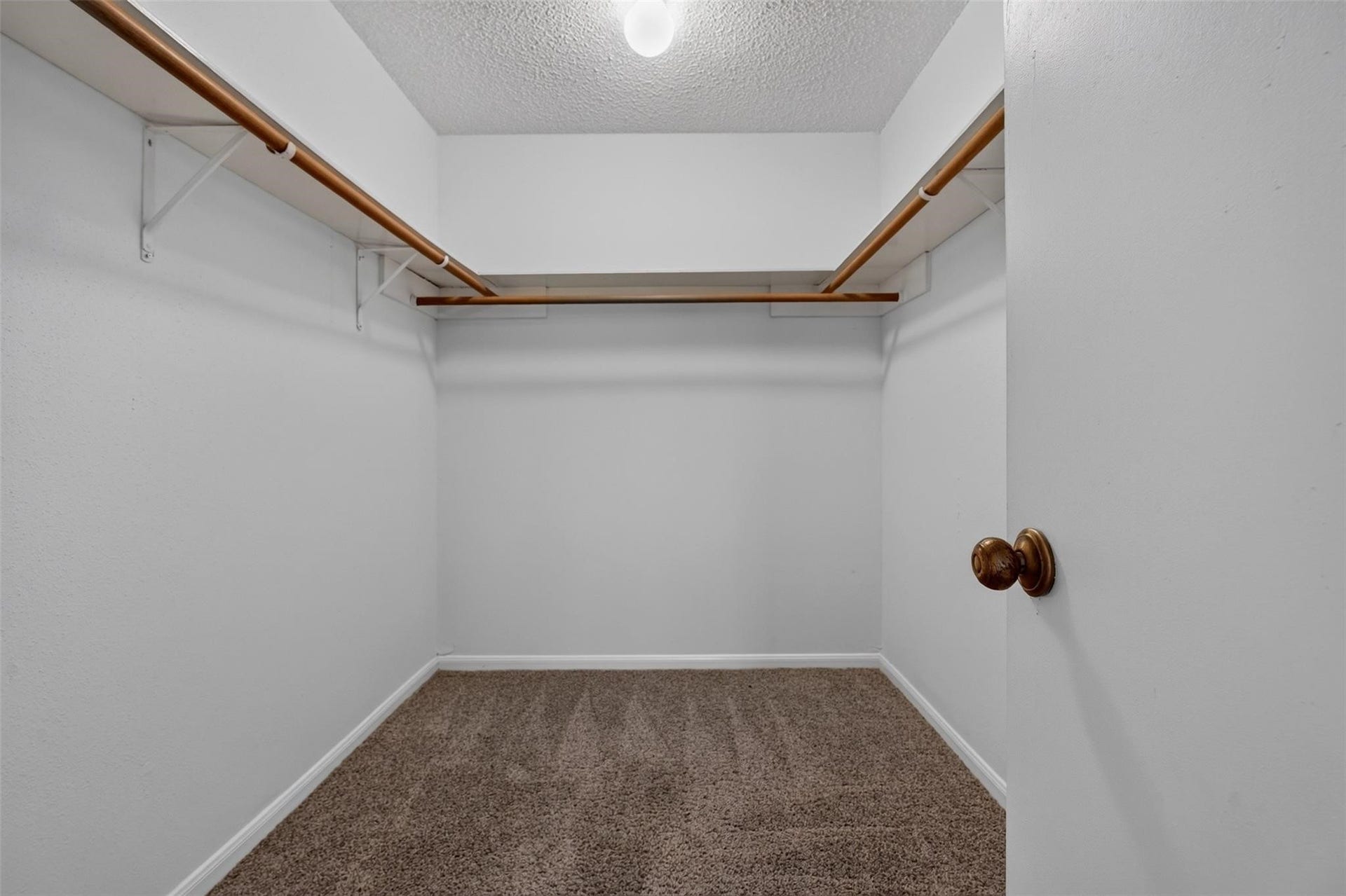 700 Thicket Lane, #304, Houston, TX 77079 Spacious walk-in closet featuring dual wooden hanging rods and plush carpet flooring, offering ample storage space.