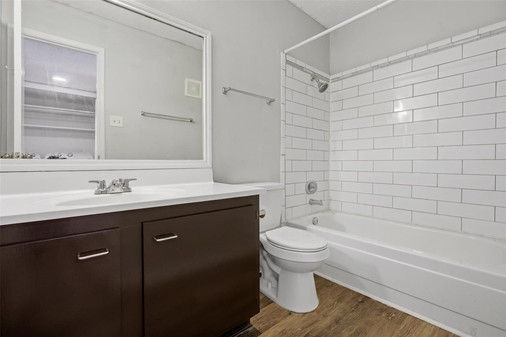 700 Thicket Lane, #304, Houston, TX 77079 Sleek bathroom with a modern vanity, large mirror, and classic white subway tile surrounding the bathtub, complemented by wood-look flooring for a warm touch.