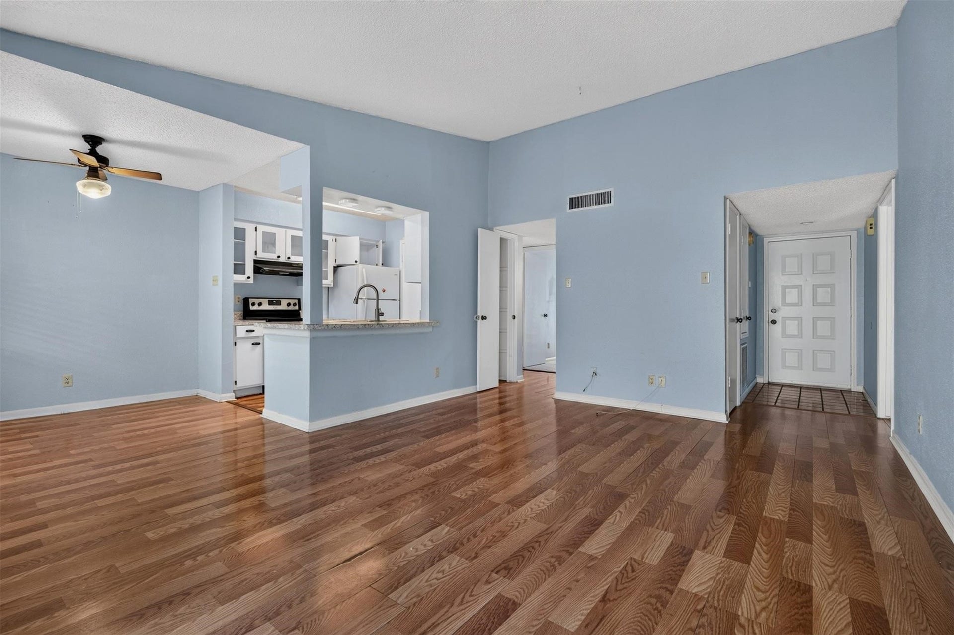 700 Thicket Lane, #304, Houston, TX 77079 Spacious living area with warm hardwood floors and soft blue walls, featuring an open kitchen with modern appliances and a convenient breakfast bar.