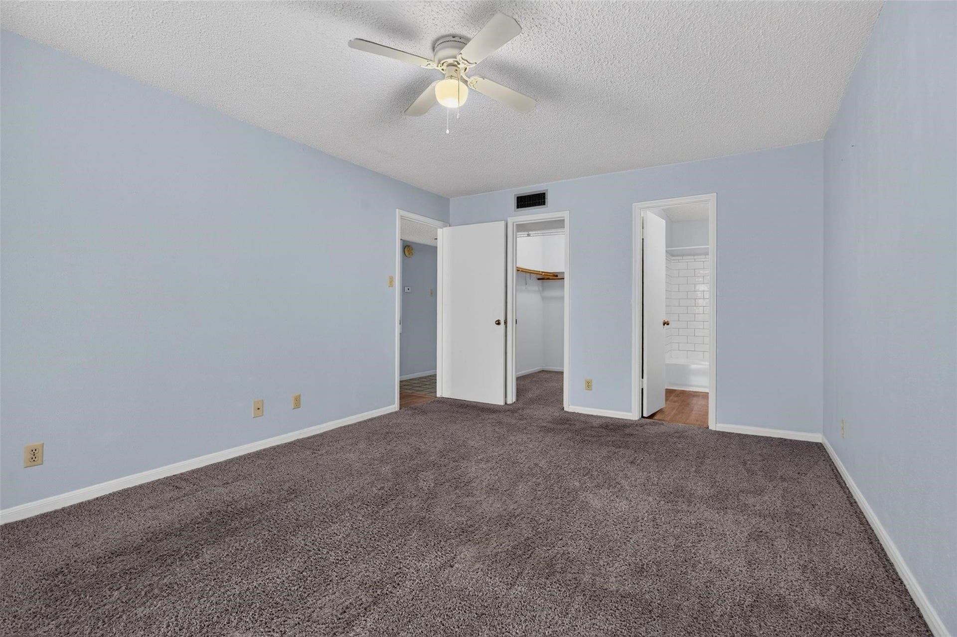 700 Thicket Lane, #304, Houston, TX 77079 Spacious bedroom with soft blue walls, plush carpeting, and a ceiling fan, featuring convenient access to a walk-in closet and ensuite bathroom.