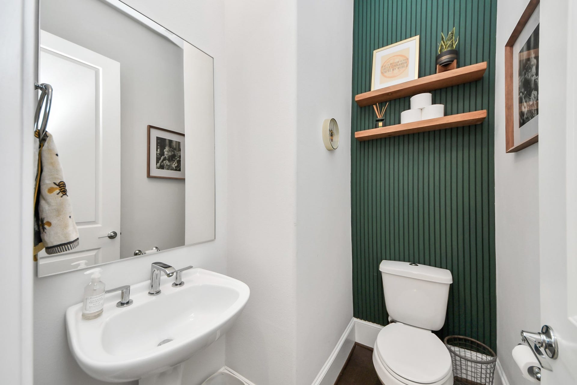 Charming powder room with a sleek pedestal sink, modern fixtures, and a stylish green accent wall featuring floating shelves for added elegance.