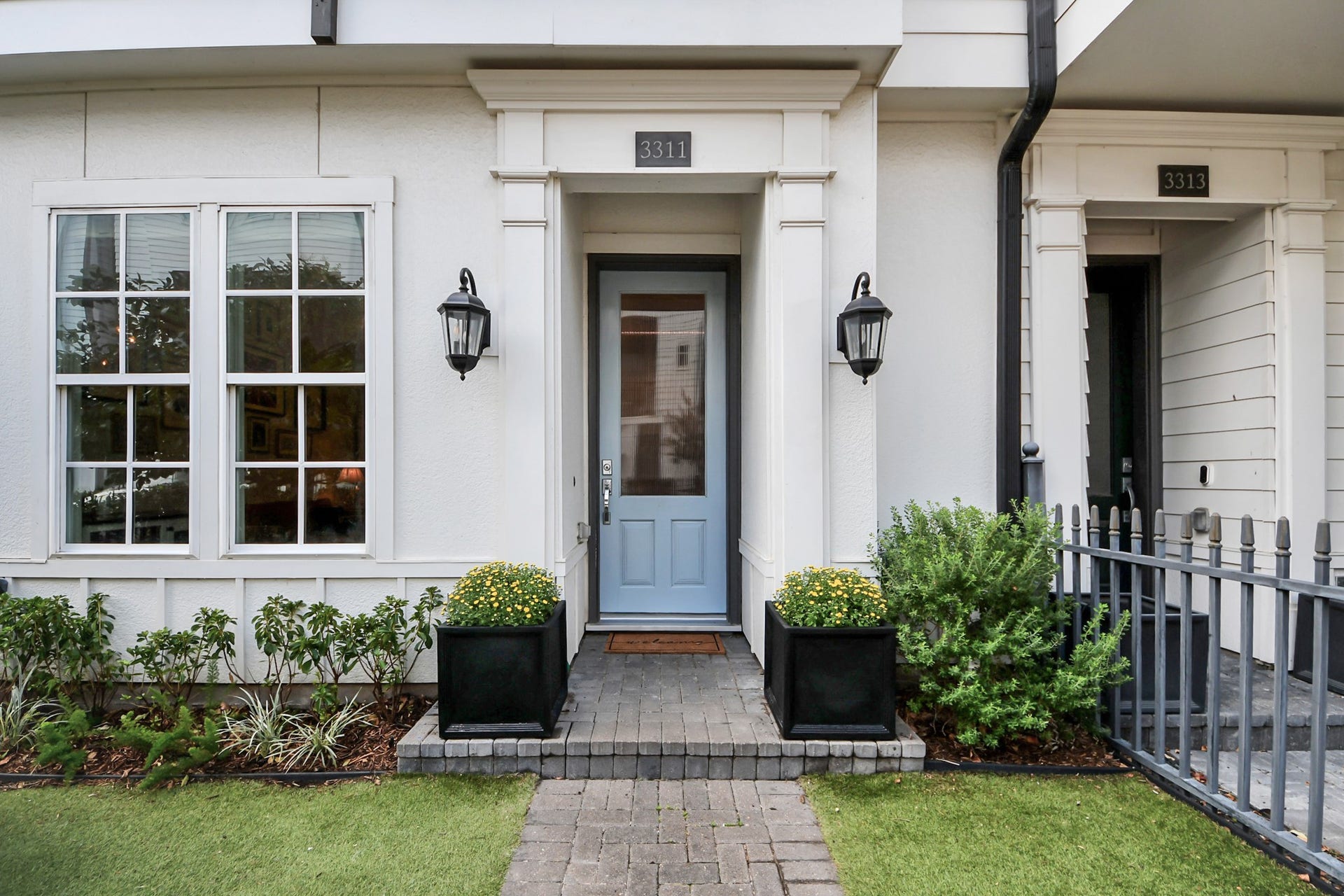 Charming entryway with a welcoming blue door, flanked by elegant lanterns and lush greenery in decorative planters.